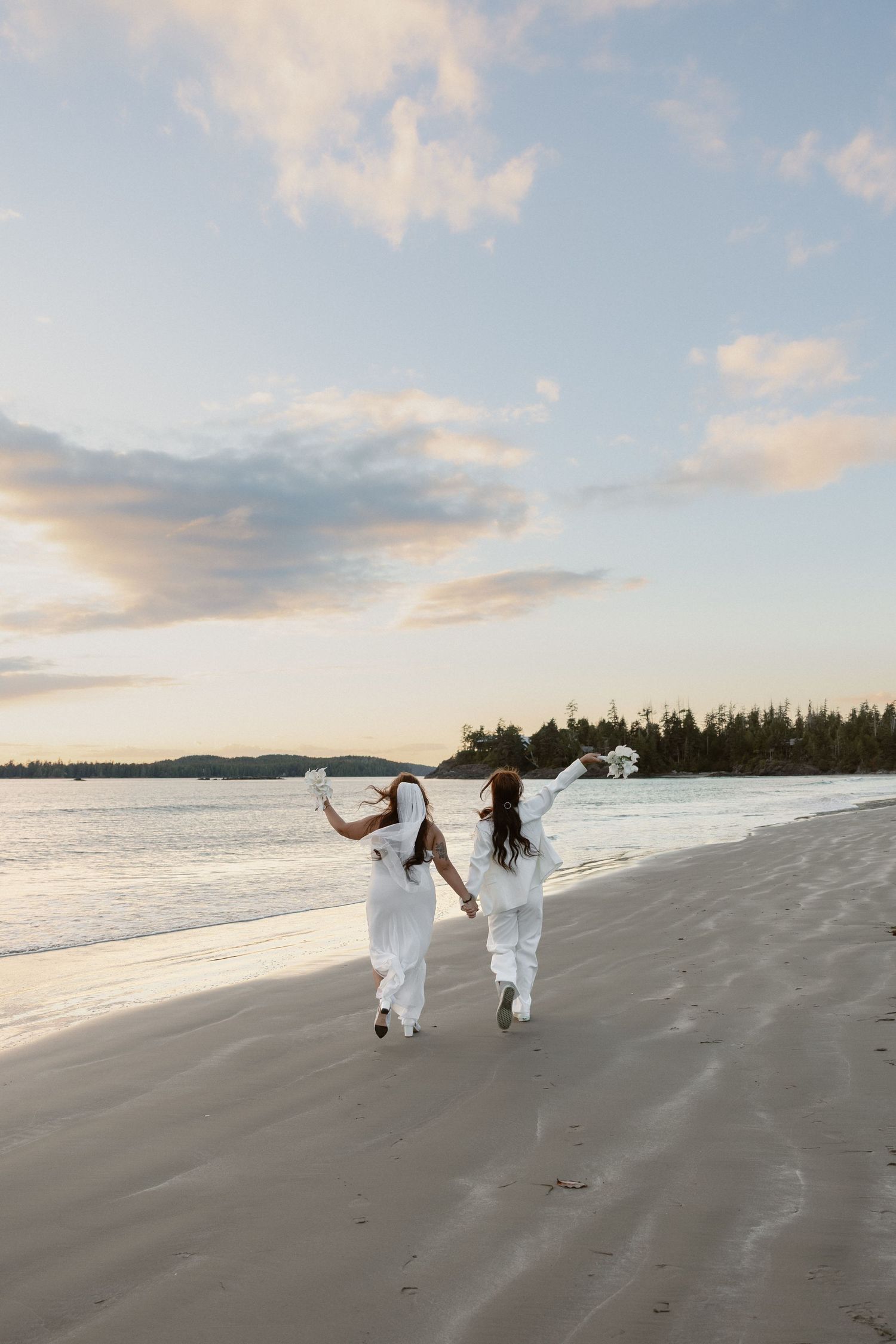 Brides in wedding dresses running joyfully along Mackenzie Beach at sunset after eloping at golden hour