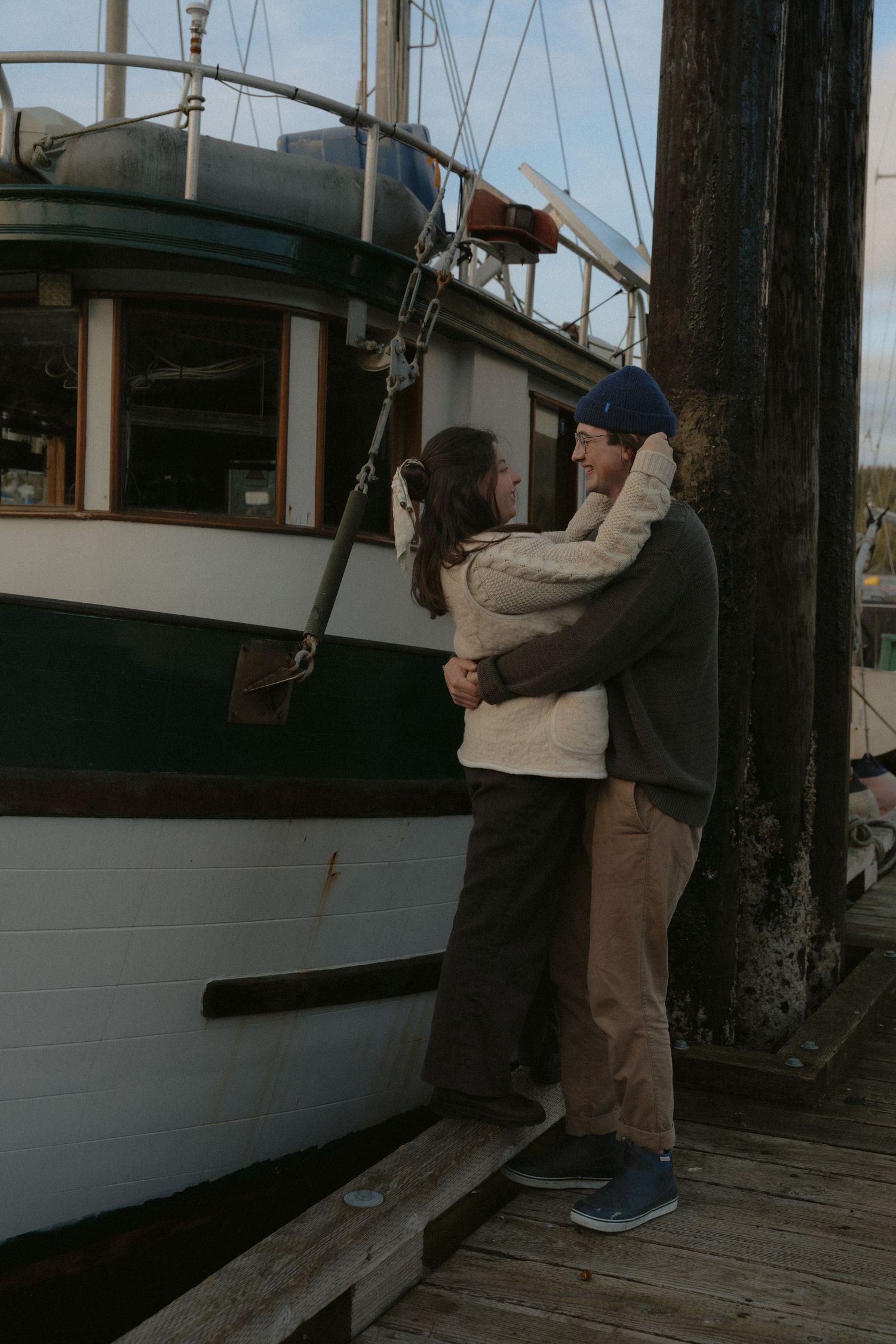 Two people share a playful moment on a wooden dock near a white boat at dusk.