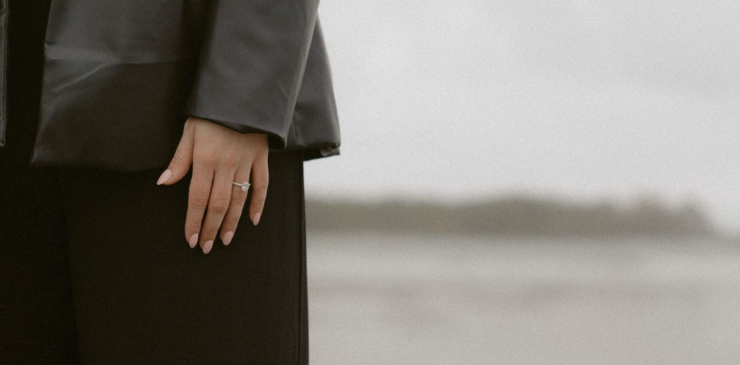 Close-up shot of a diamond engagement ring on a hand against Chesterman Beach