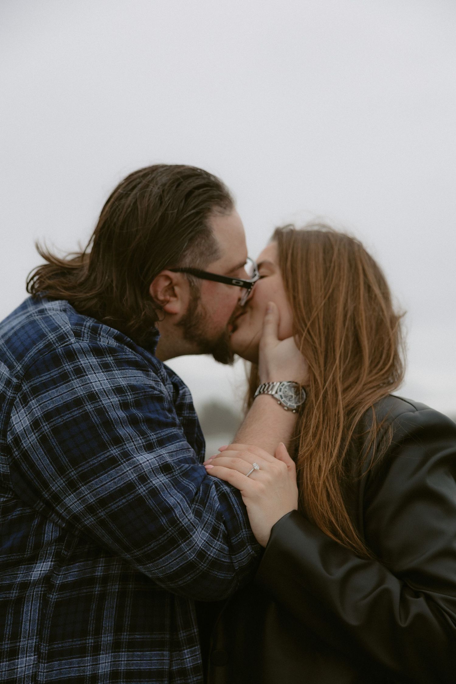 Romantic embrace between couple wearing plaid and black against overcast sky on Chesterman Beach, Tofino