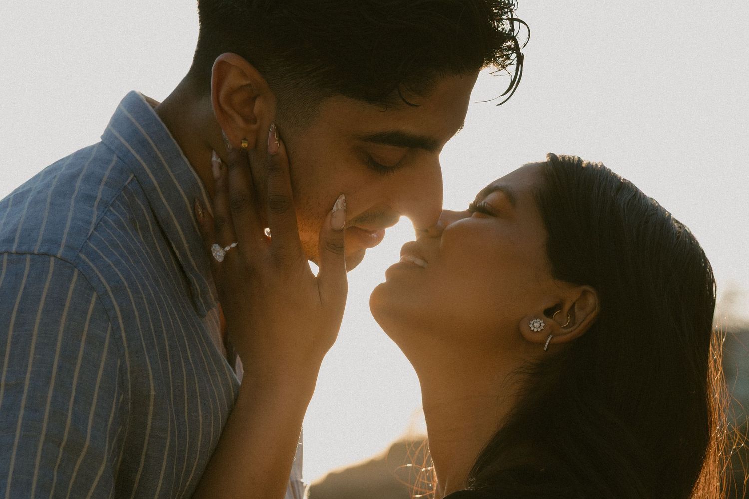 Couple sharing a tender moment at golden hour, foreheads nearly touching in warm sunlight.