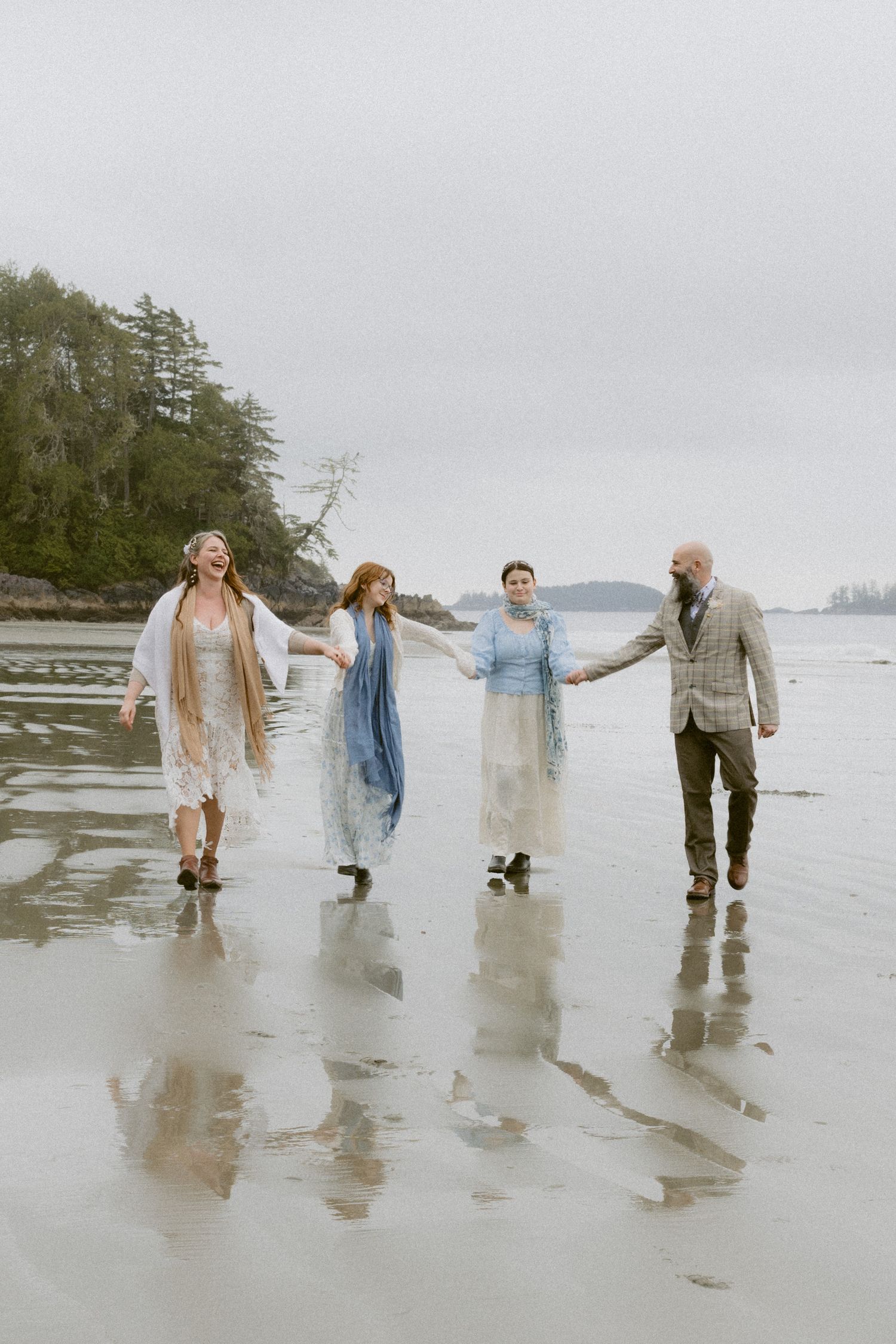A group walks playfully along a misty Pacific Northwest beach with waves reflecting in wet sand.