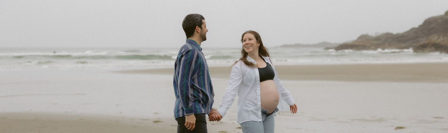 Couple walking together on a foggy beach during maternity photoshoot.
