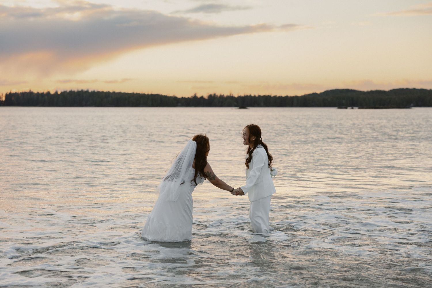 Tofino elopement couple of two brides holding hands in calm waters at sunset