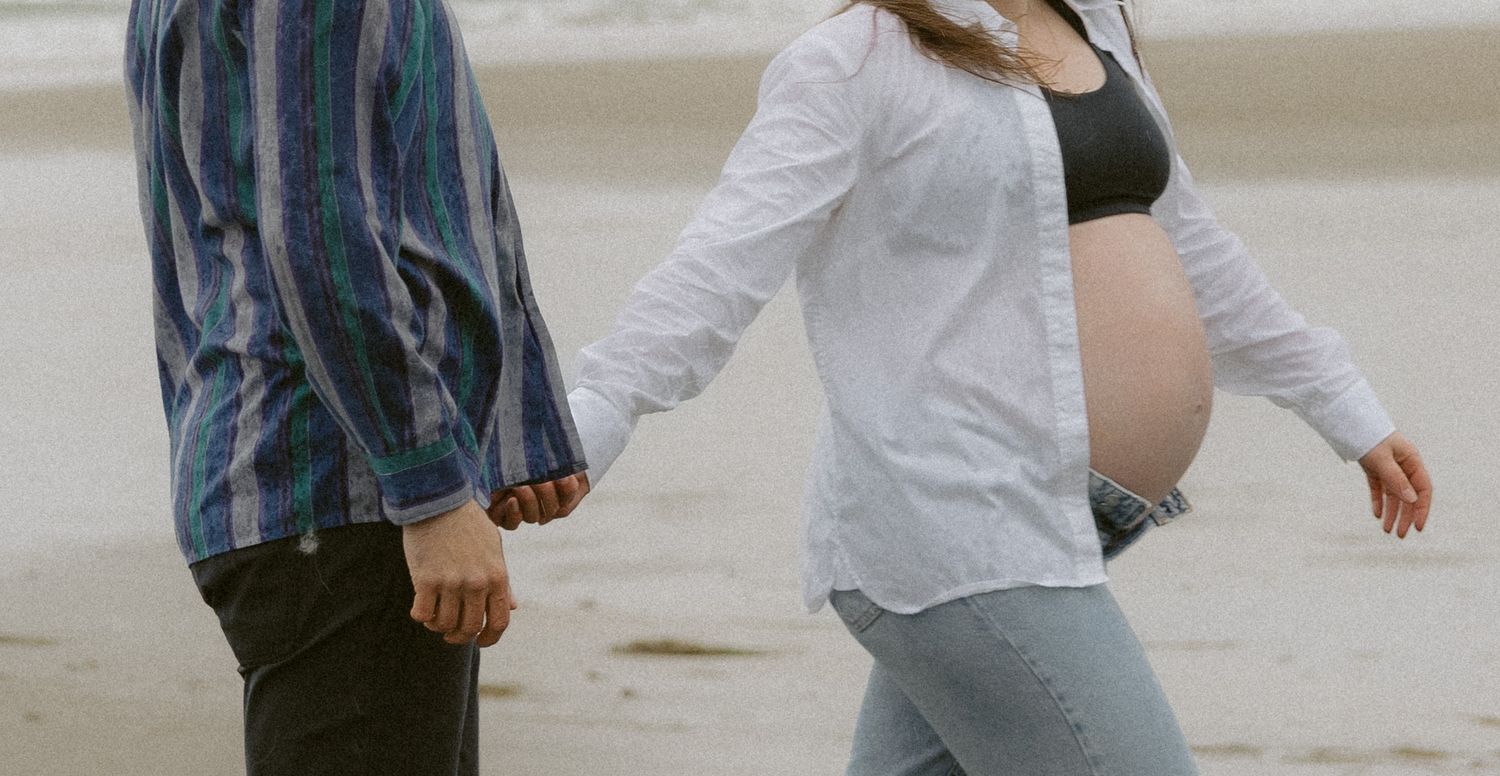 Couple strolling hand in hand on a sandy beach during an overcast day.