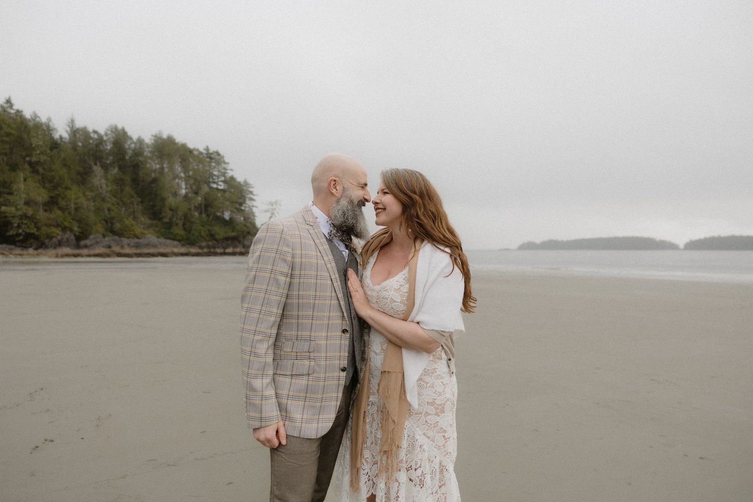 A couple strolls hand in hand on a moody Pacific Northwest beach with islands in the distance.