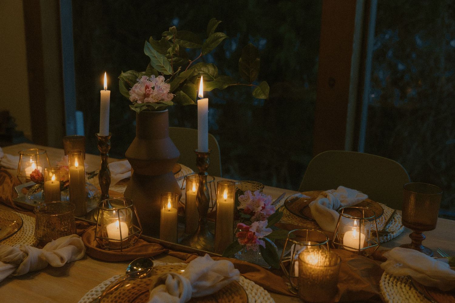 An elegant table setting with glowing candles and pink flowers in a dark, romantic atmosphere.