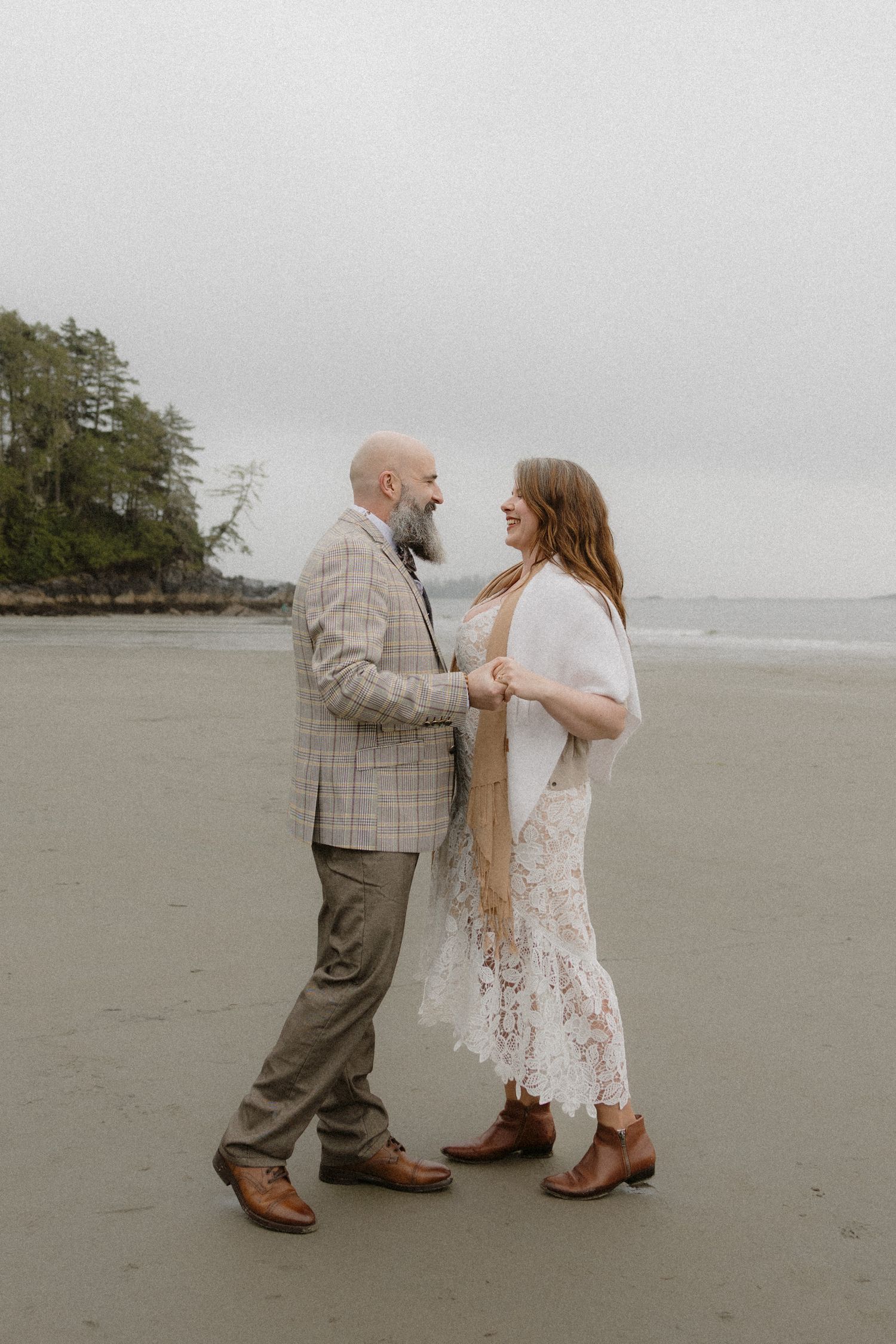 A couple in wedding attire sharing a romantic moment on a misty beach.