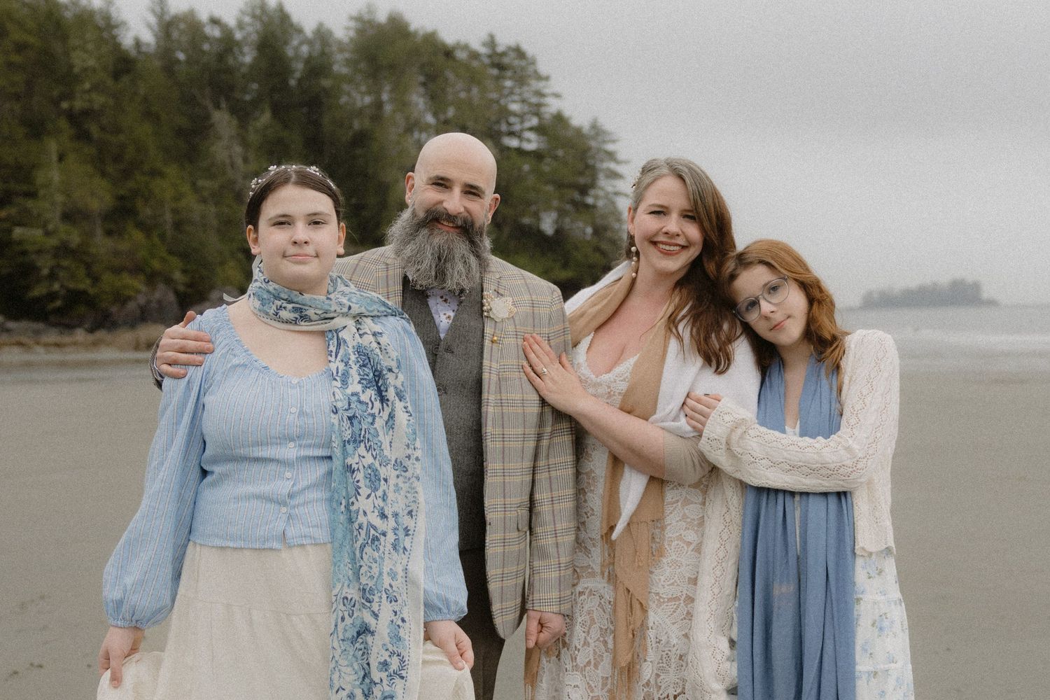Wedding party poses together on misty Pacific Northwest beach wearing coordinated blue and neutral tones.