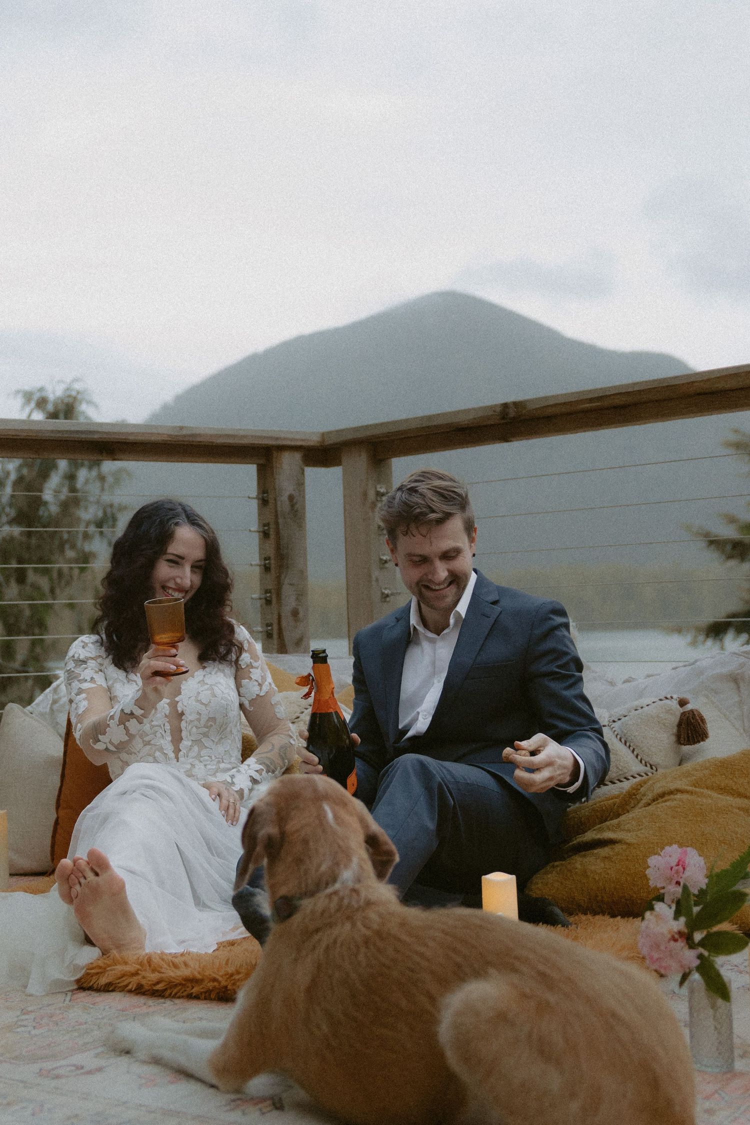Couple relaxes on blankets with their dogs against a mountainous backdrop.