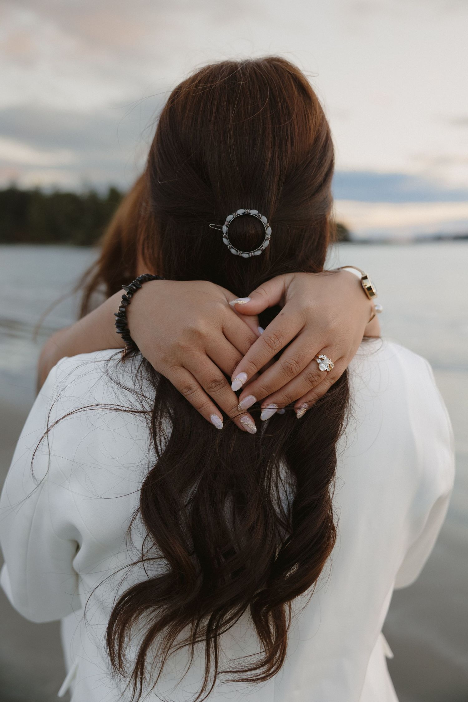 Close-up of hands with rings and a decorative hair clip against an ocean backdrop.