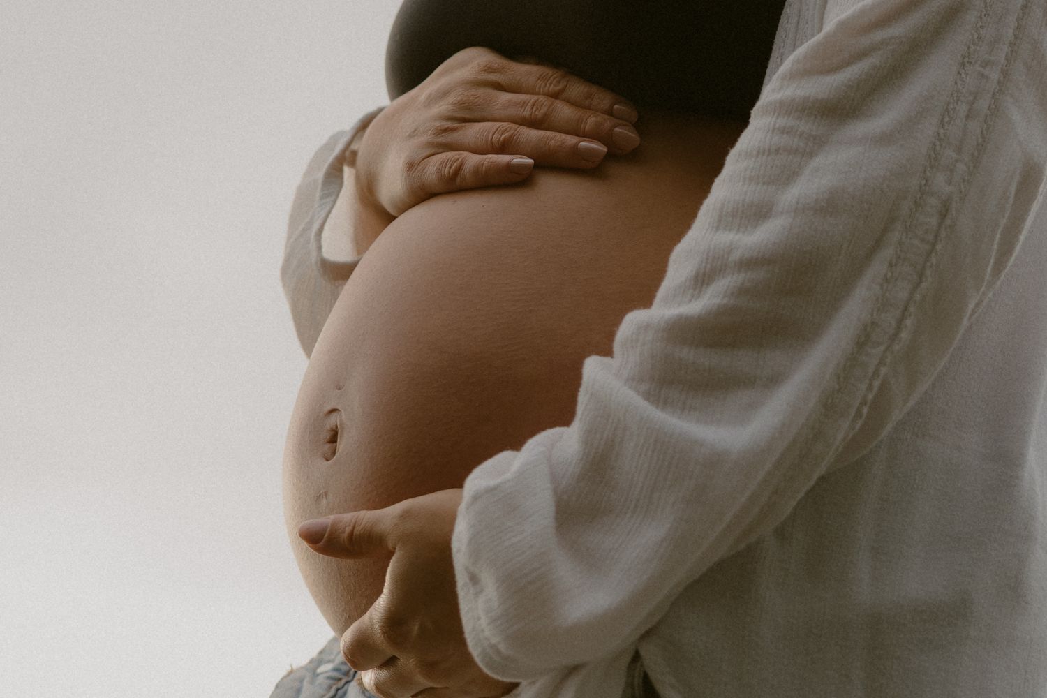 Close-up maternity photos highlighting pregnant belly against light background.
