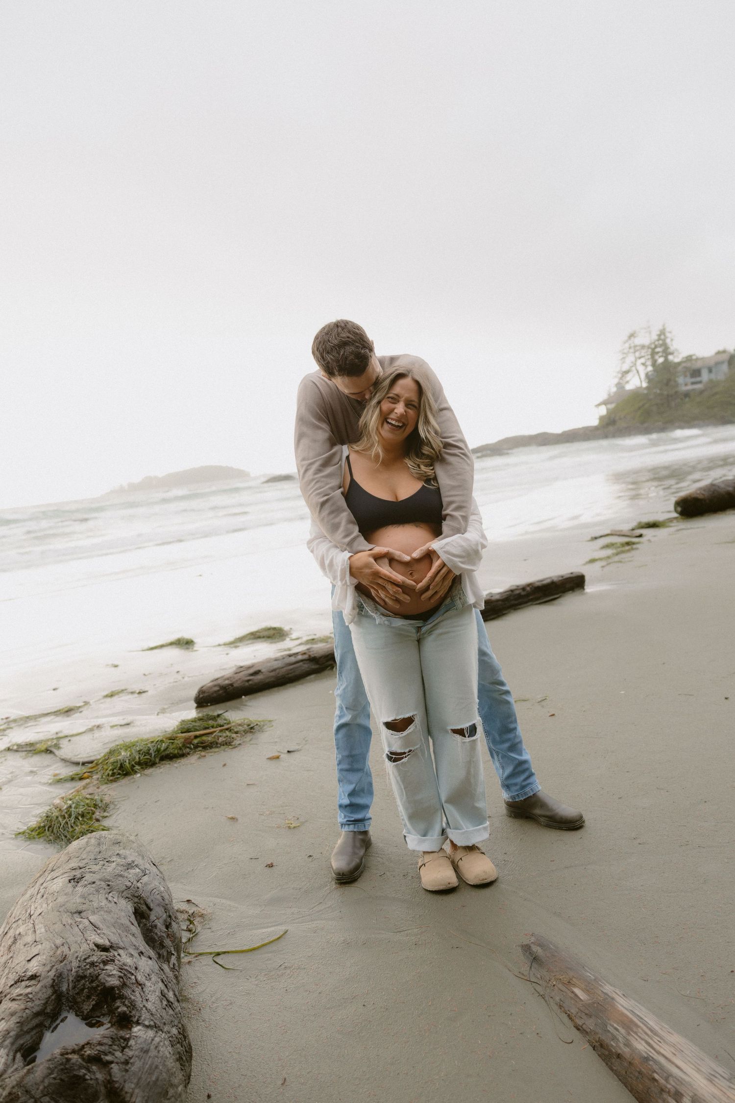 A couple sits together on driftwood at a foggy beach during an intimate photoshoot.