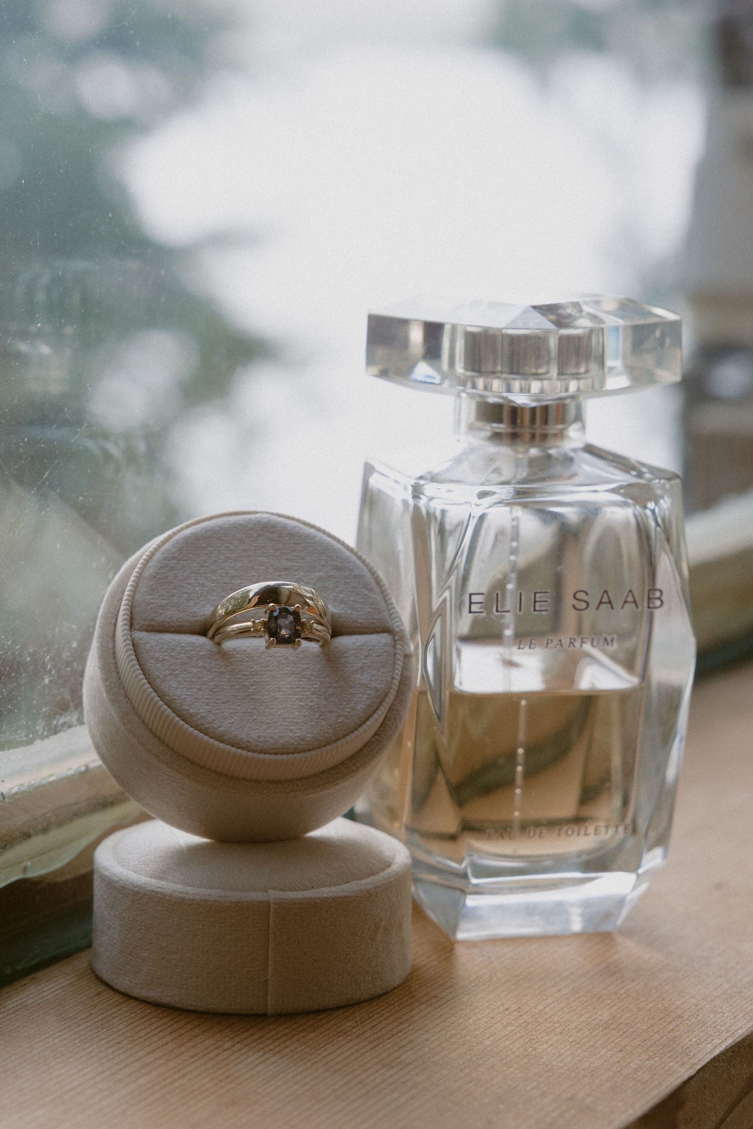Perfume bottles and wedding rings arranged on a wooden surface in natural light.