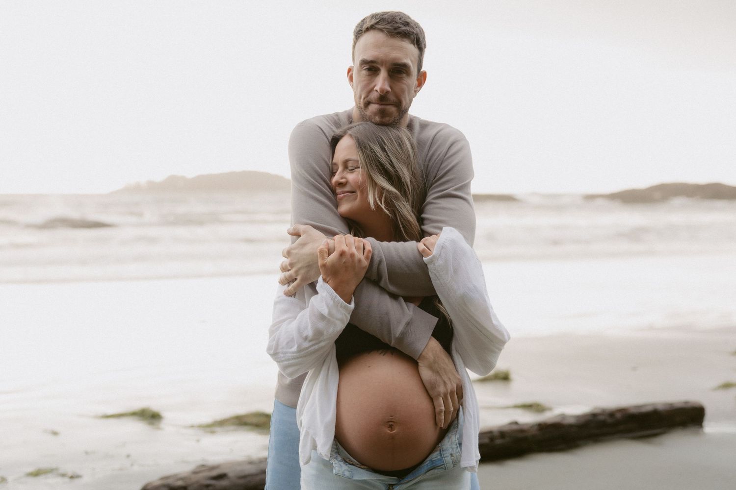 Loving embrace during maternity photo session on cloudy beach.