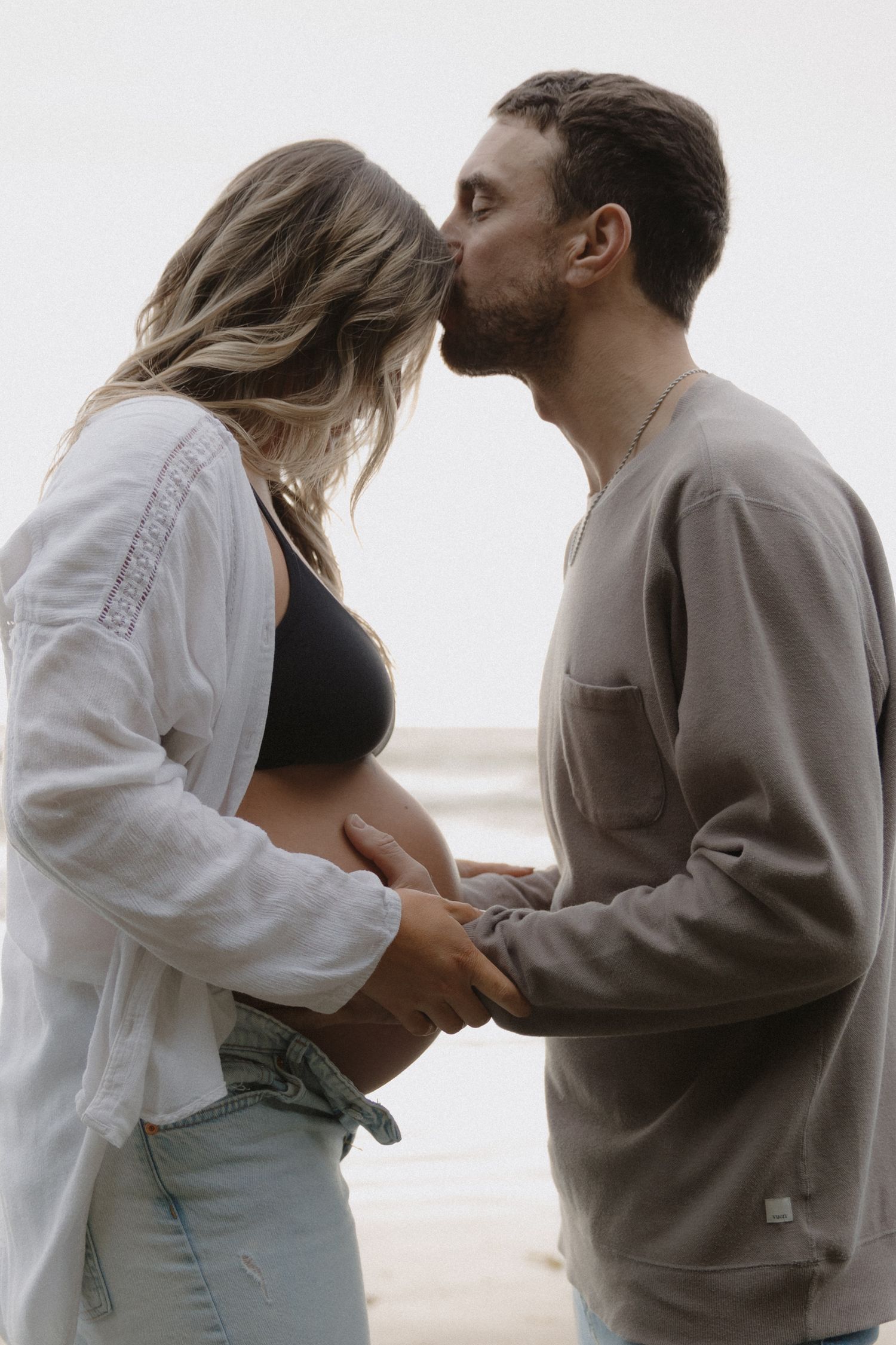 Intimate moment between couple during beachside maternity photoshoot.