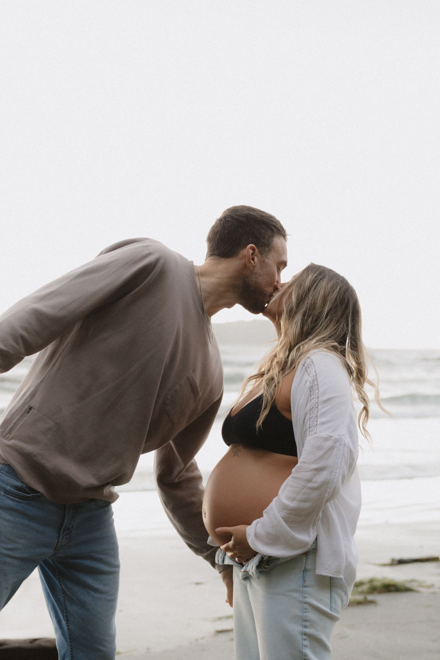 Romantic maternity photoshoot at beach with couple embracing and showing baby bump.
