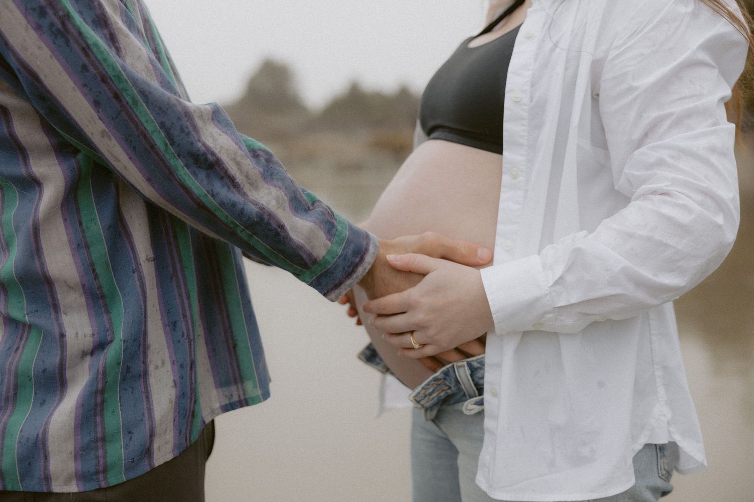 Intimate maternity photo showing hands cradling a pregnant belly on a beach.