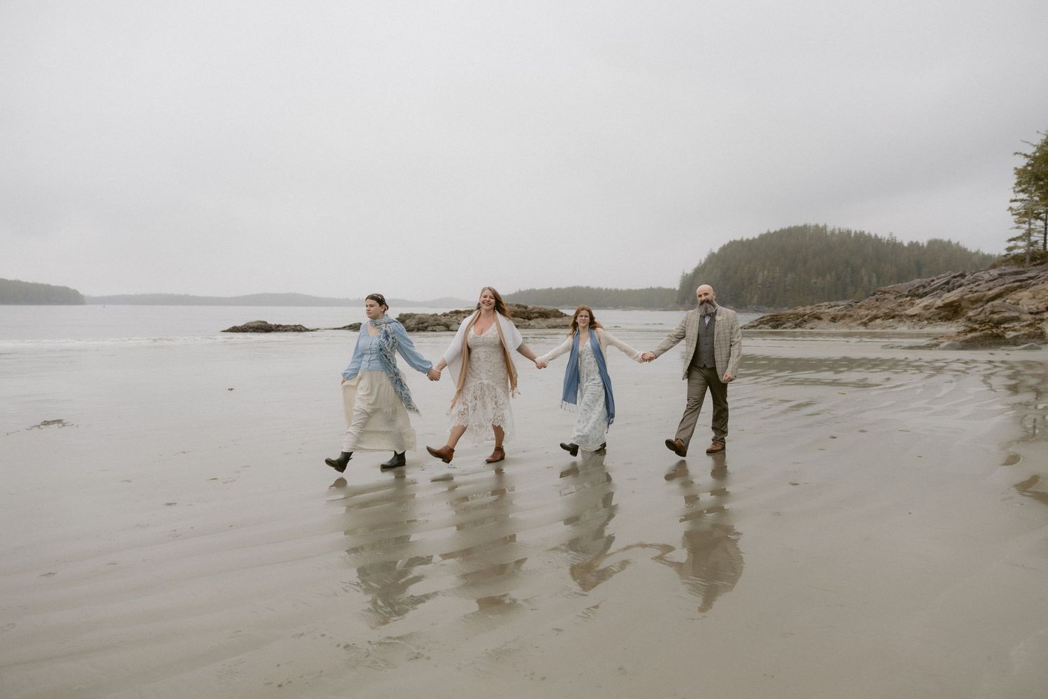 People holding hands while walking in a line on a foggy beach.