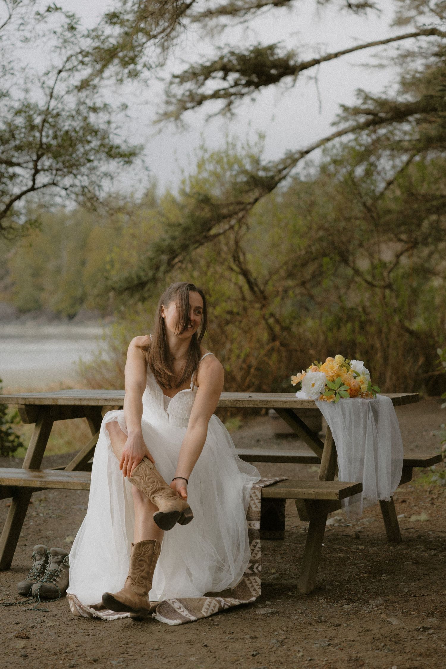 Tofino bride in white dress putting on her boots at Bella Pacifica Campground rustic wooden bench