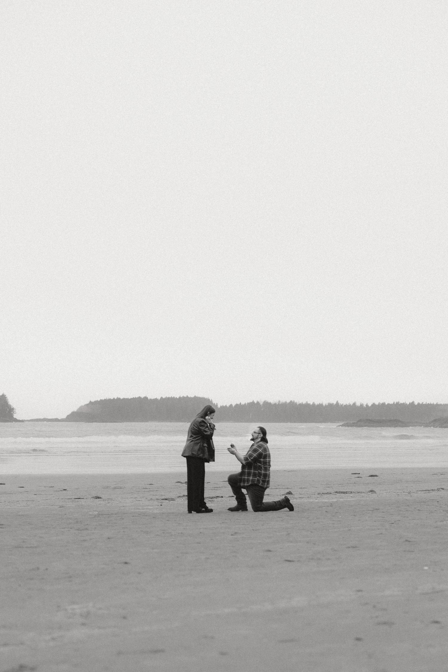 Silhouettes of two people on a vast empty beach with forested headlands in the distance.