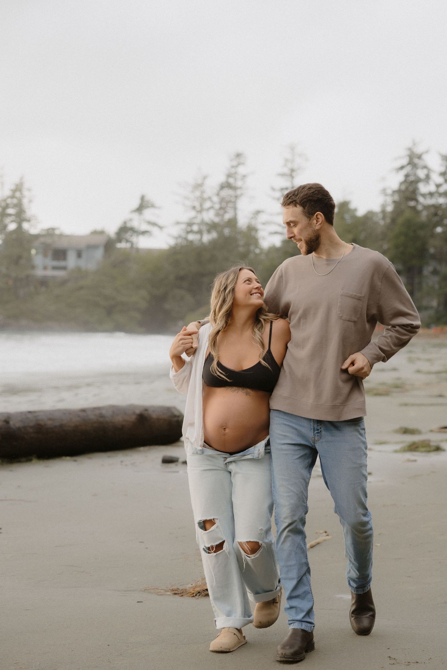 A couple walks hand in hand along a misty Pacific Northwest beach.