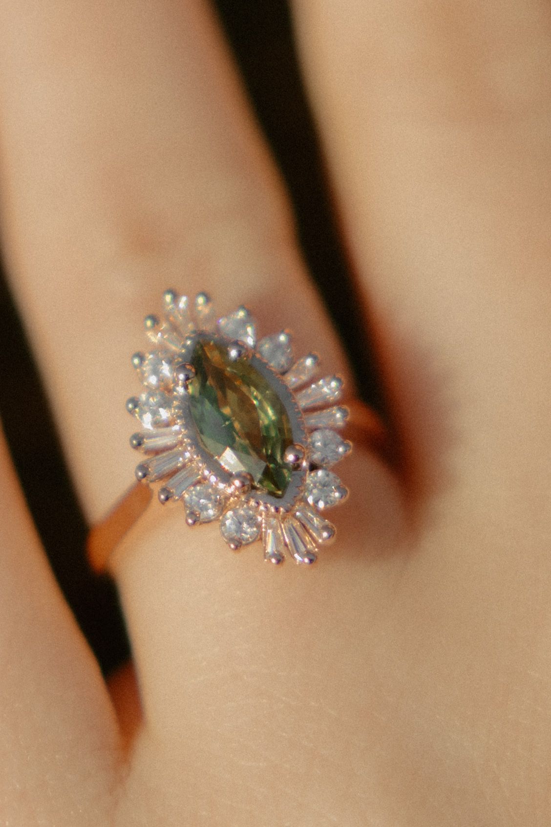 Rose gold ring featuring a marquise green gemstone center surrounded by a halo of baguette and round diamonds.