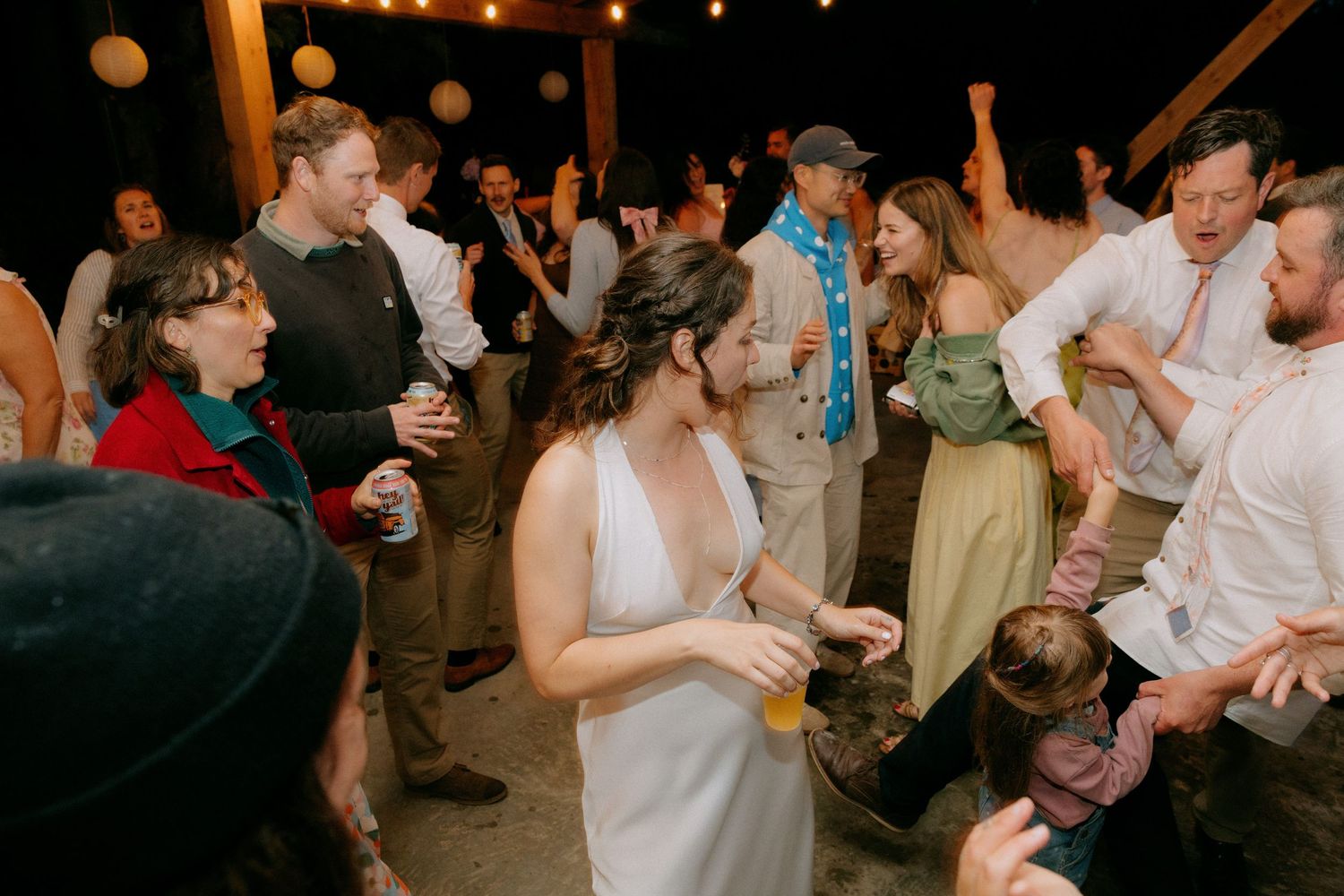 Bride in white dress dancing joyfully with wedding guests at a lively indoor reception celebration.