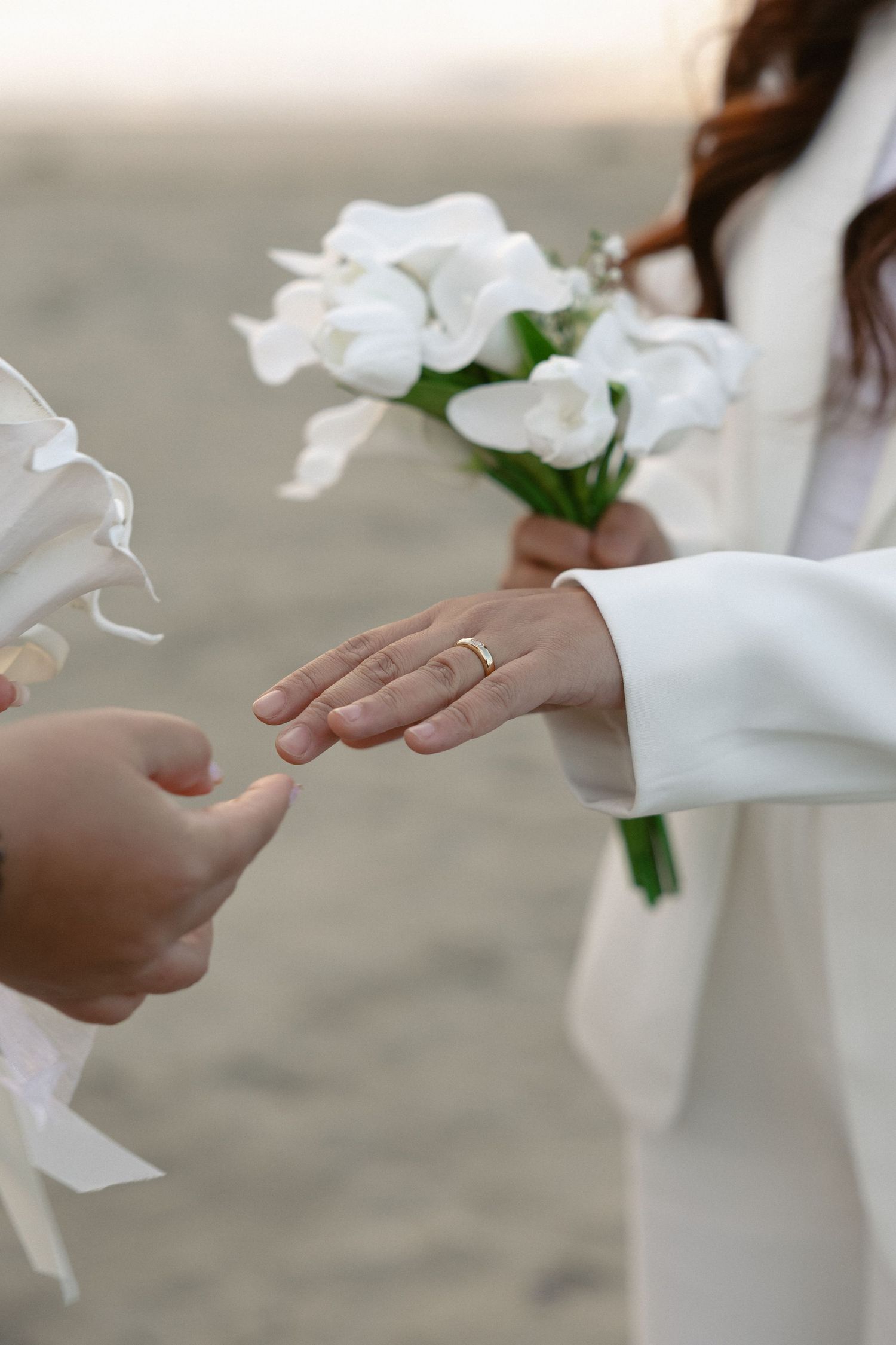 Close-up of hands exchanging a white floral bouquet on a sandy beach.