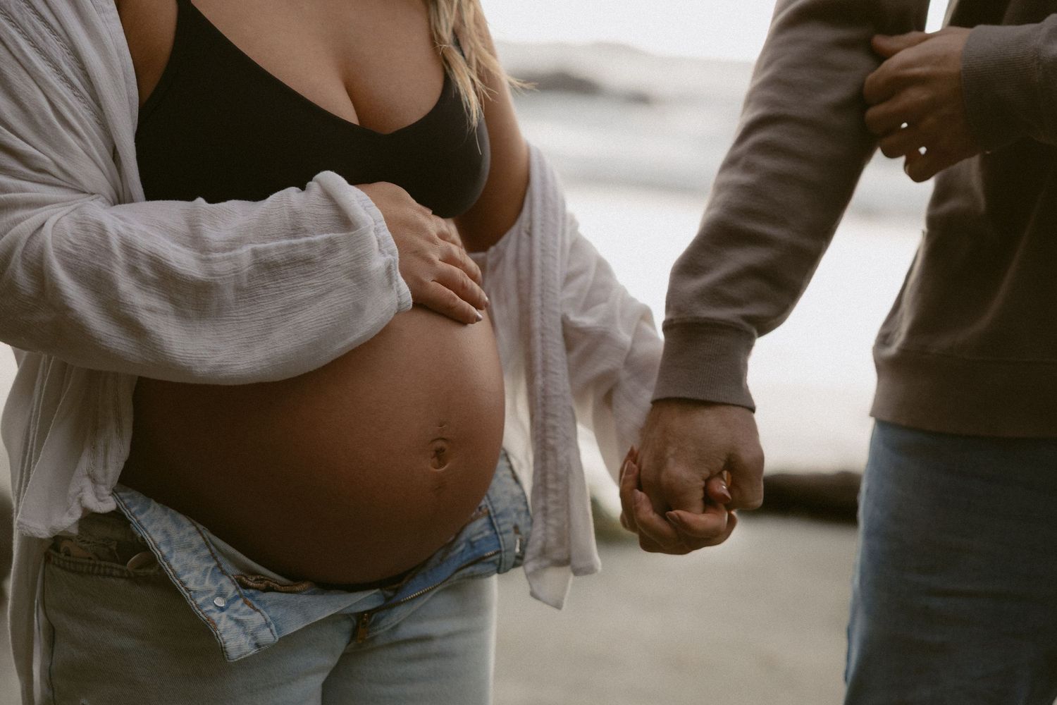 Tofino maternity couple holding hands with a visible pregnant belly on Chesterman Beach