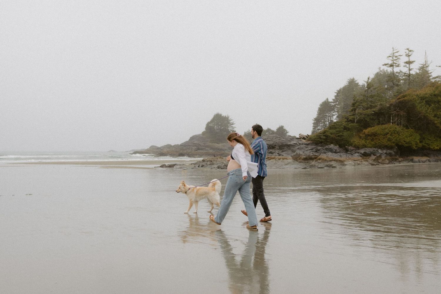 People walking together along a misty Pacific Northwest beach with rocky cliffs in the background.