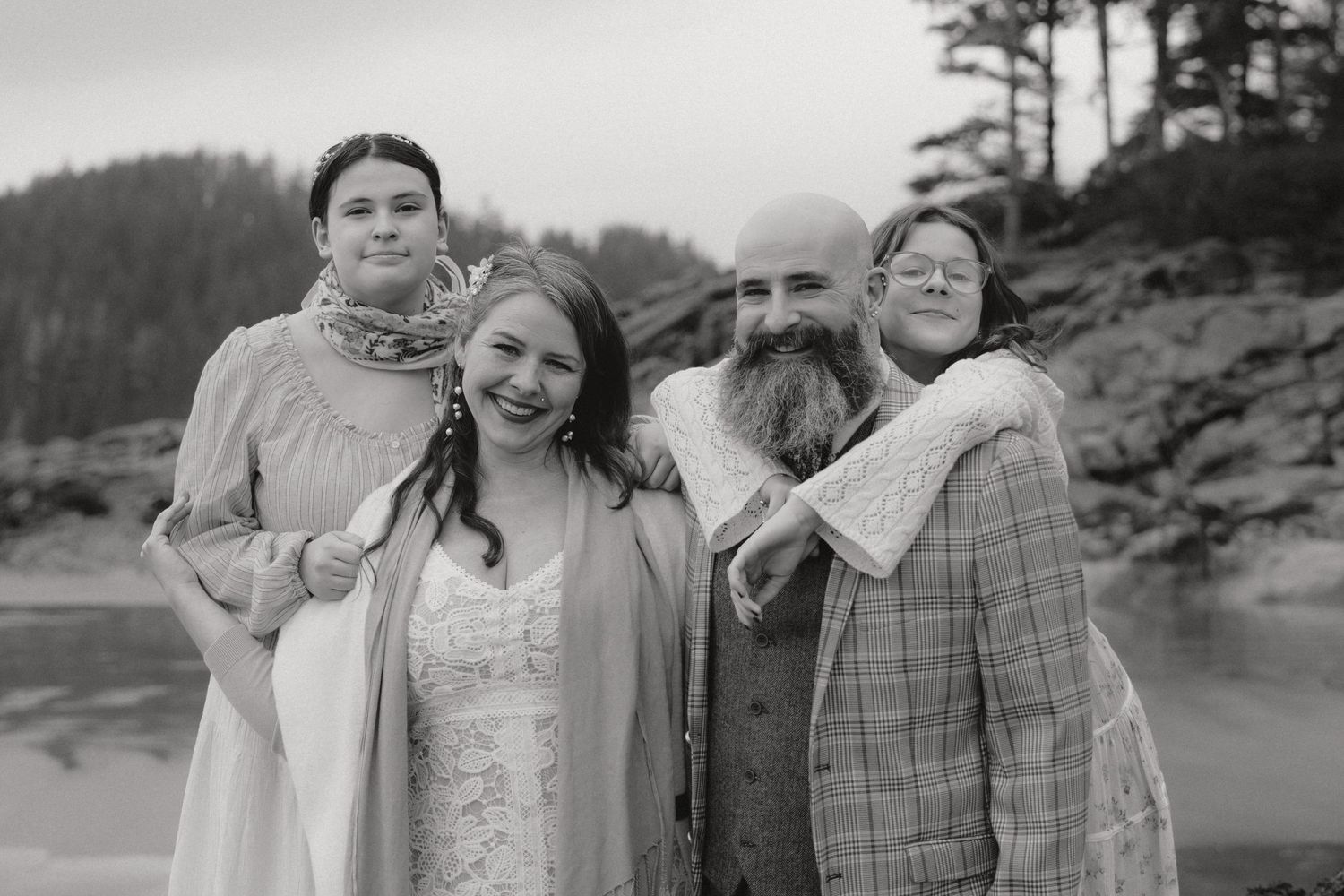 Wedding party sharing a candid laughing moment together outdoors with evergreen trees in the background.