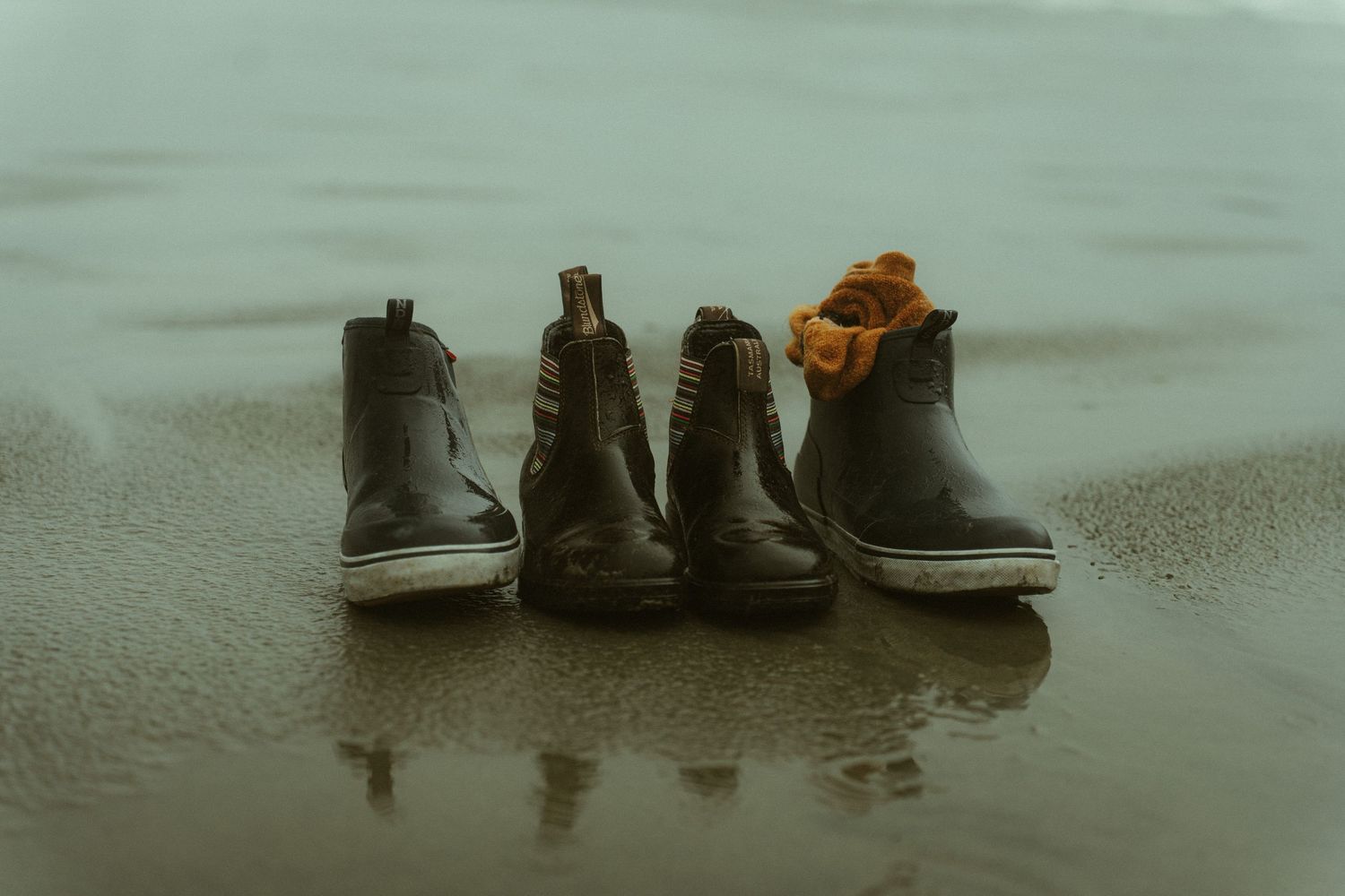 Shoes and reflections line up along the edge of a wet beach at sunset