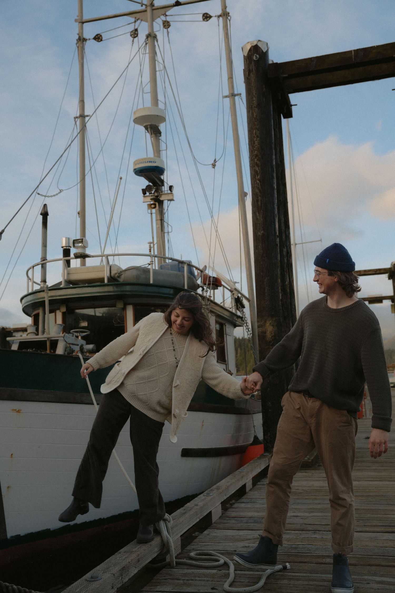 People interact casually on a marina dock with boats and cloudy skies in the background.