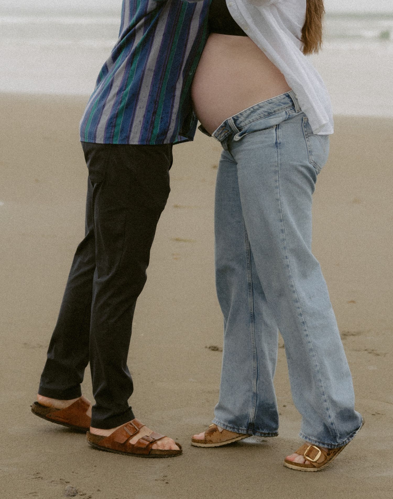Close-up view of feet dancing on a beach, showing two people in jeans and brown shoes stepping together.