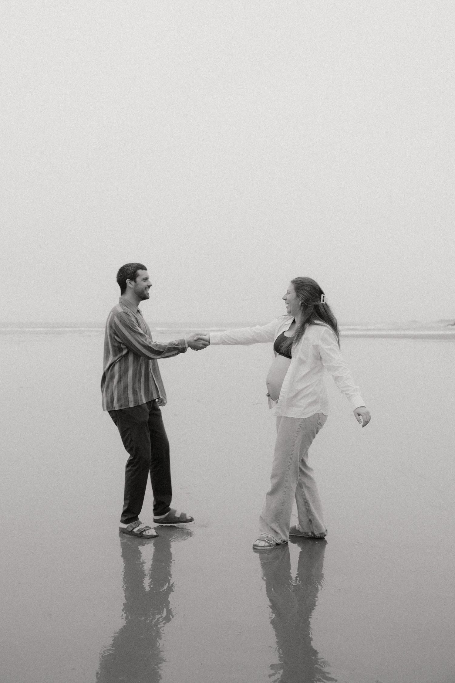 A couple dances playfully on a misty beach in black and white.