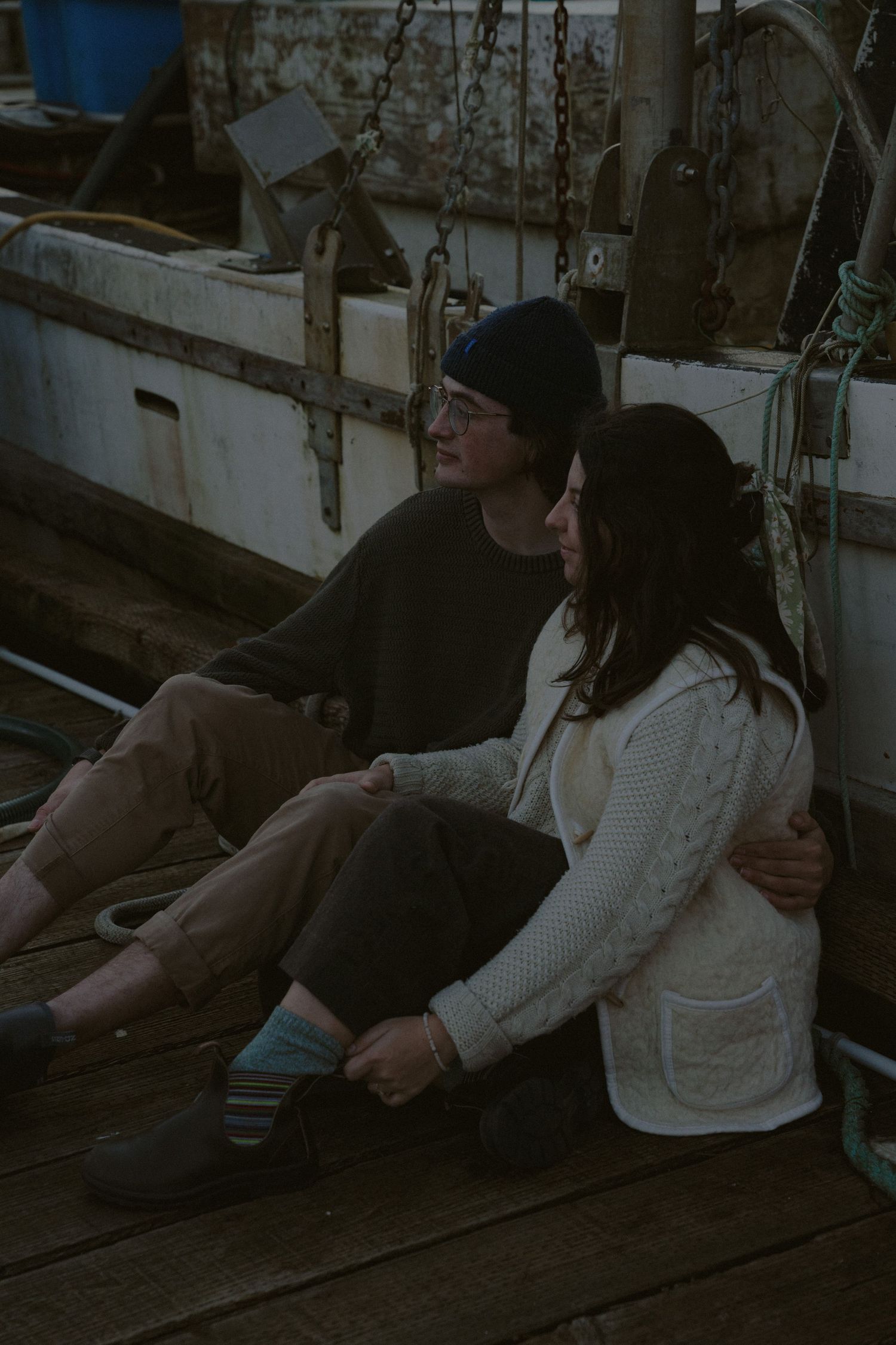 Two people lounging on wooden dock at marina during evening.