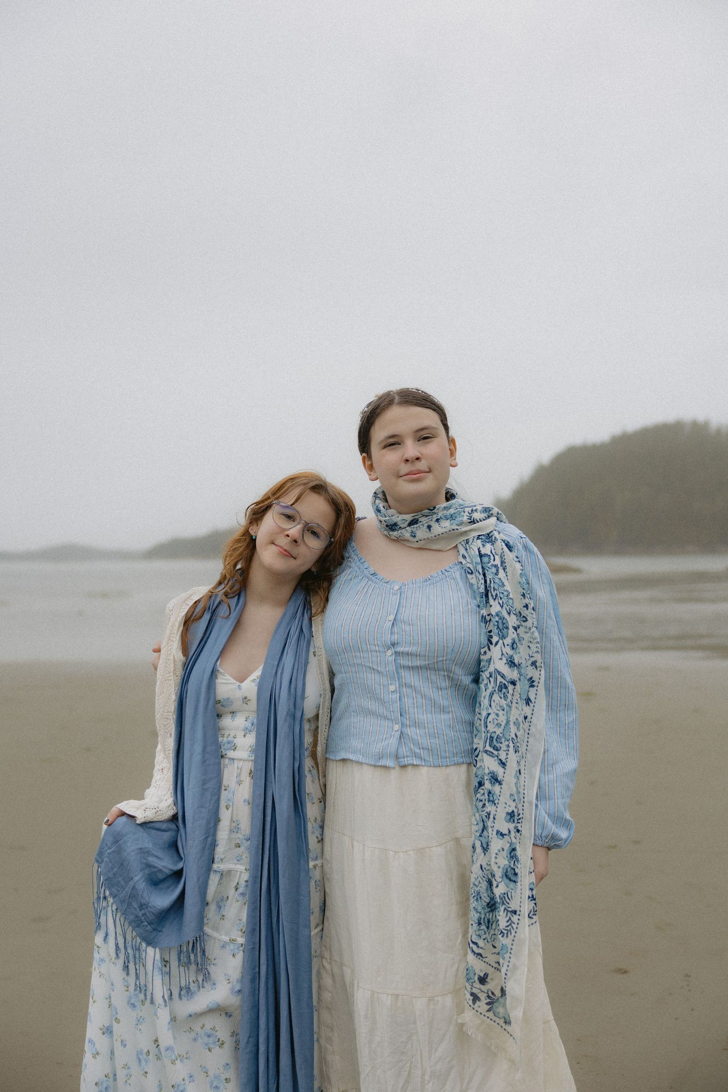 Two people in coordinating blue and white outfits embrace on foggy beach.