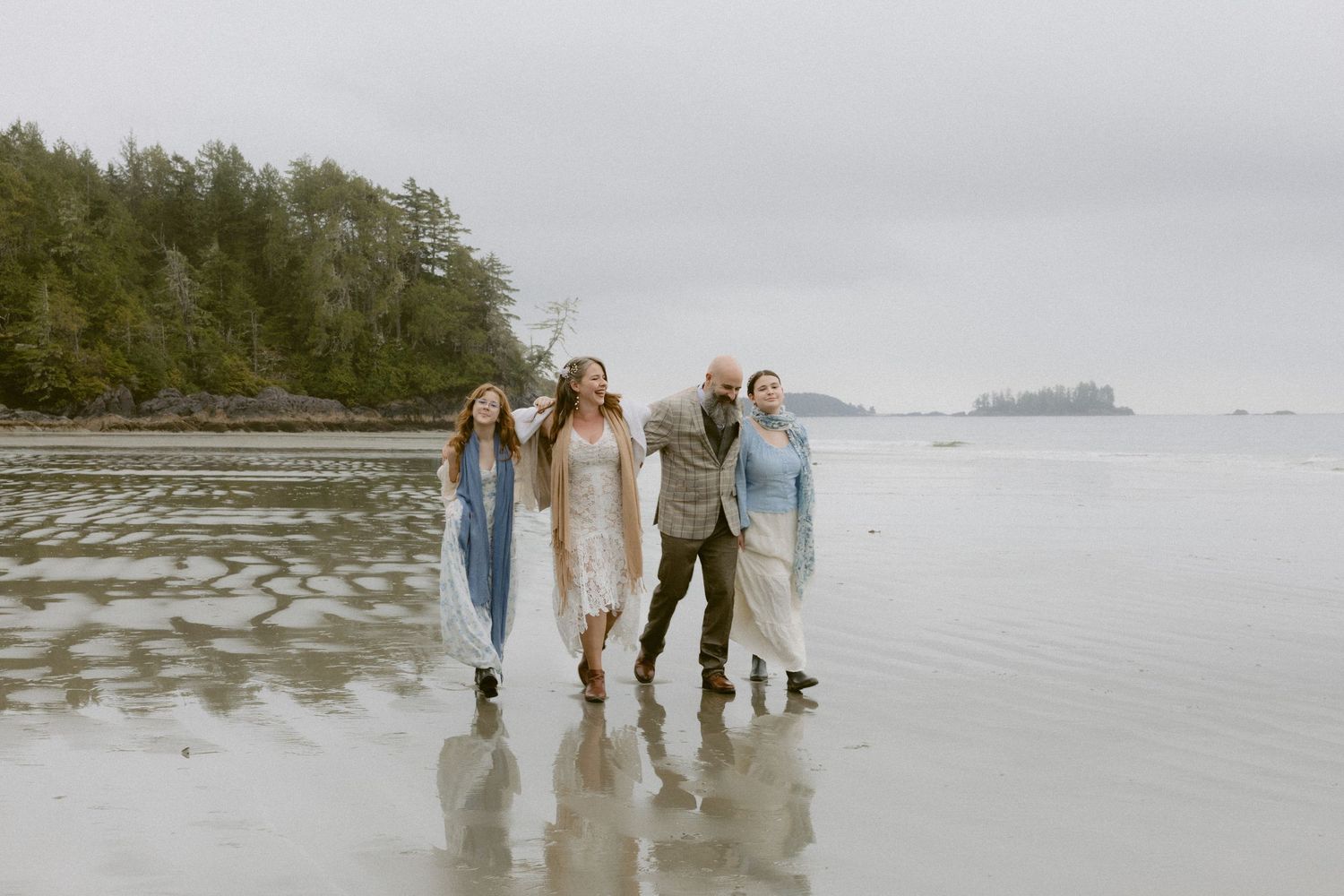A group walking together on a misty beach with evergreen trees in the background.