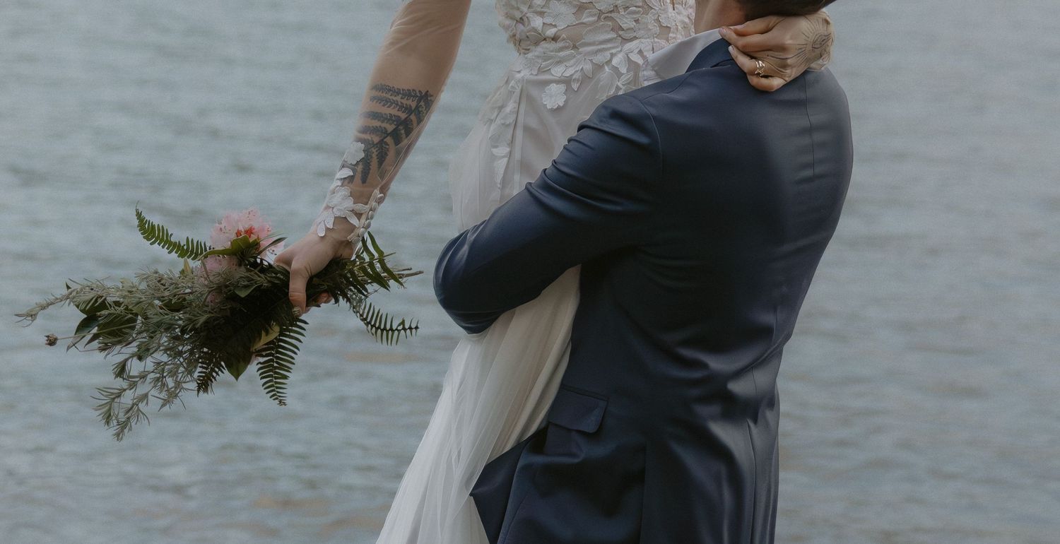 A romantic moment captured between a couple on a rocky beach with mountains in the distance.