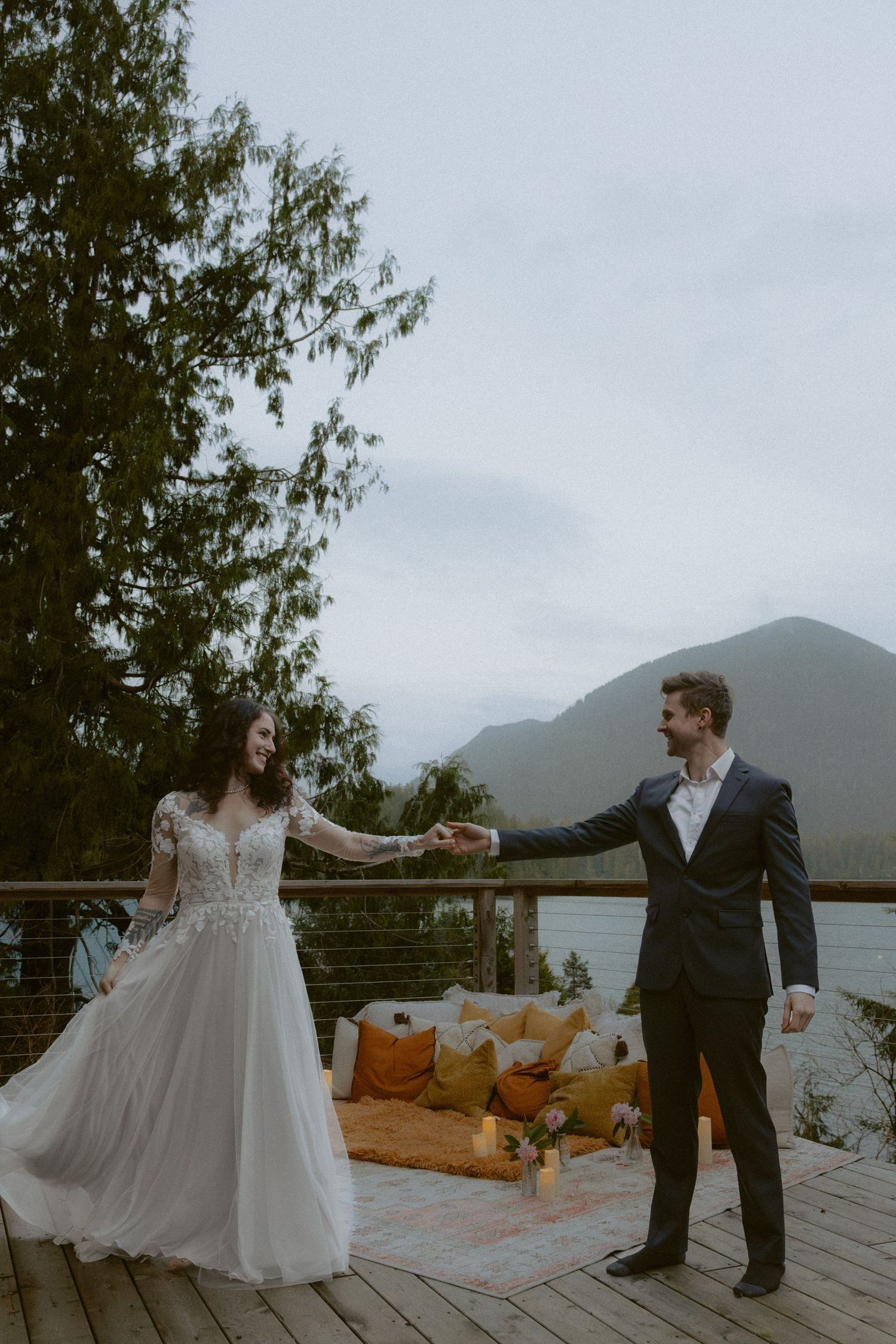 Newlyweds share a romantic dance on a lakeside deck with mountains and autumn decor visible.