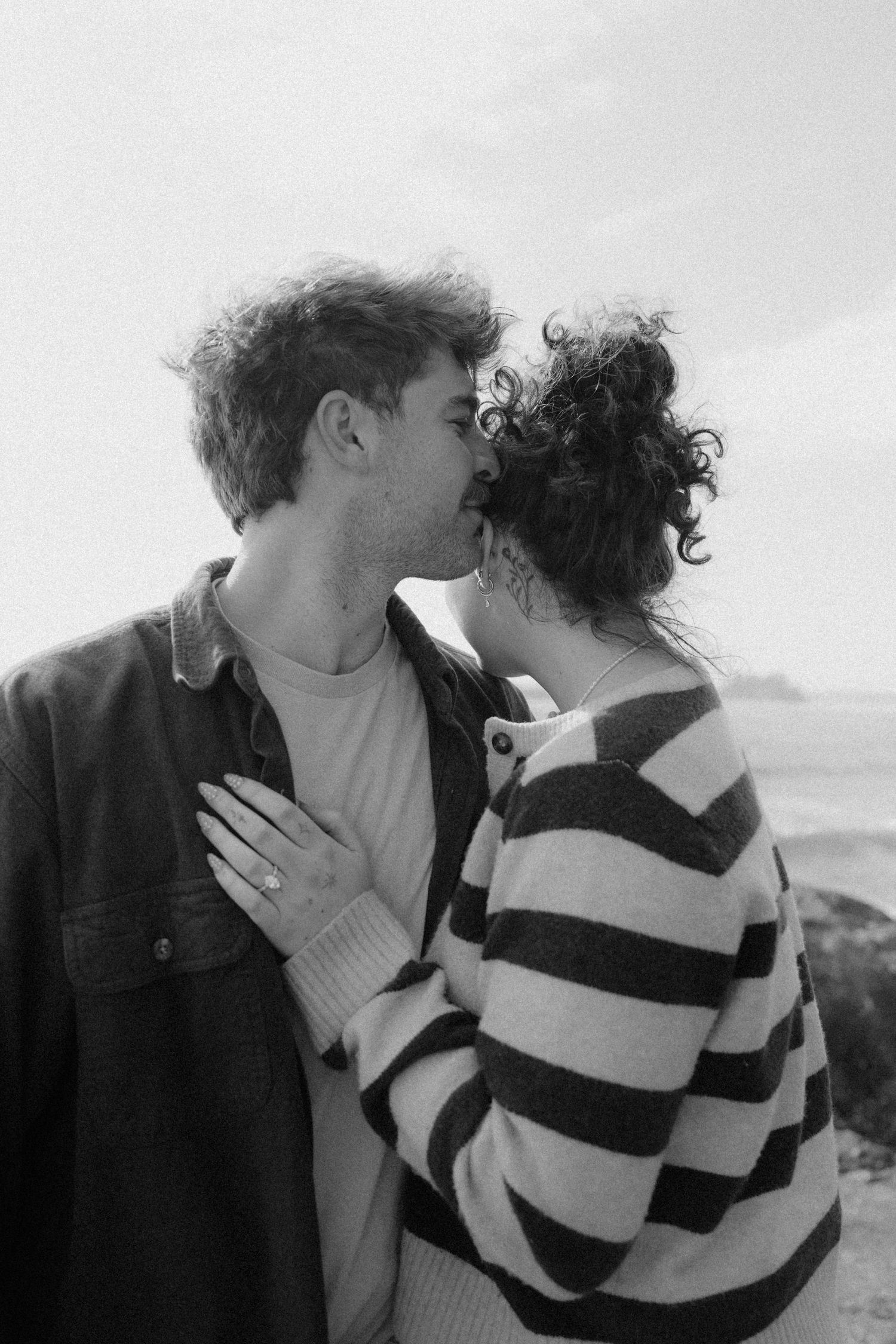 Black and white photo of couple sharing a tender kiss on rocky coastal cliffside.