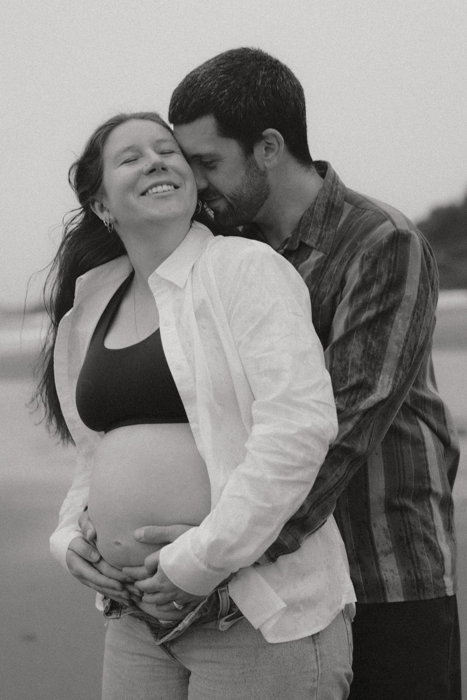 Black and white maternity photo of a couple embracing on the beach.
