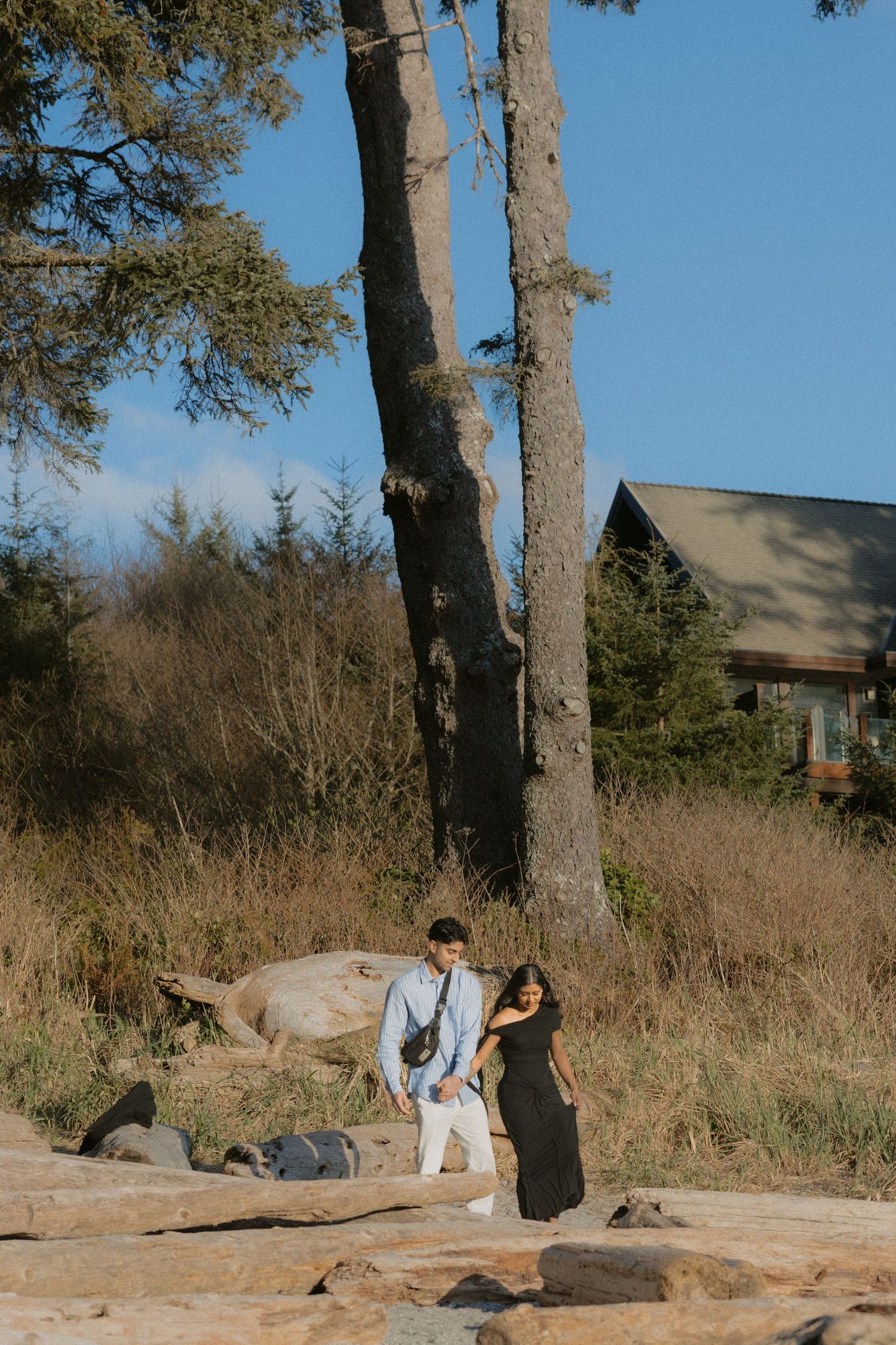 Couple standing together near large trees and rocks in a natural outdoor setting on a sunny day.