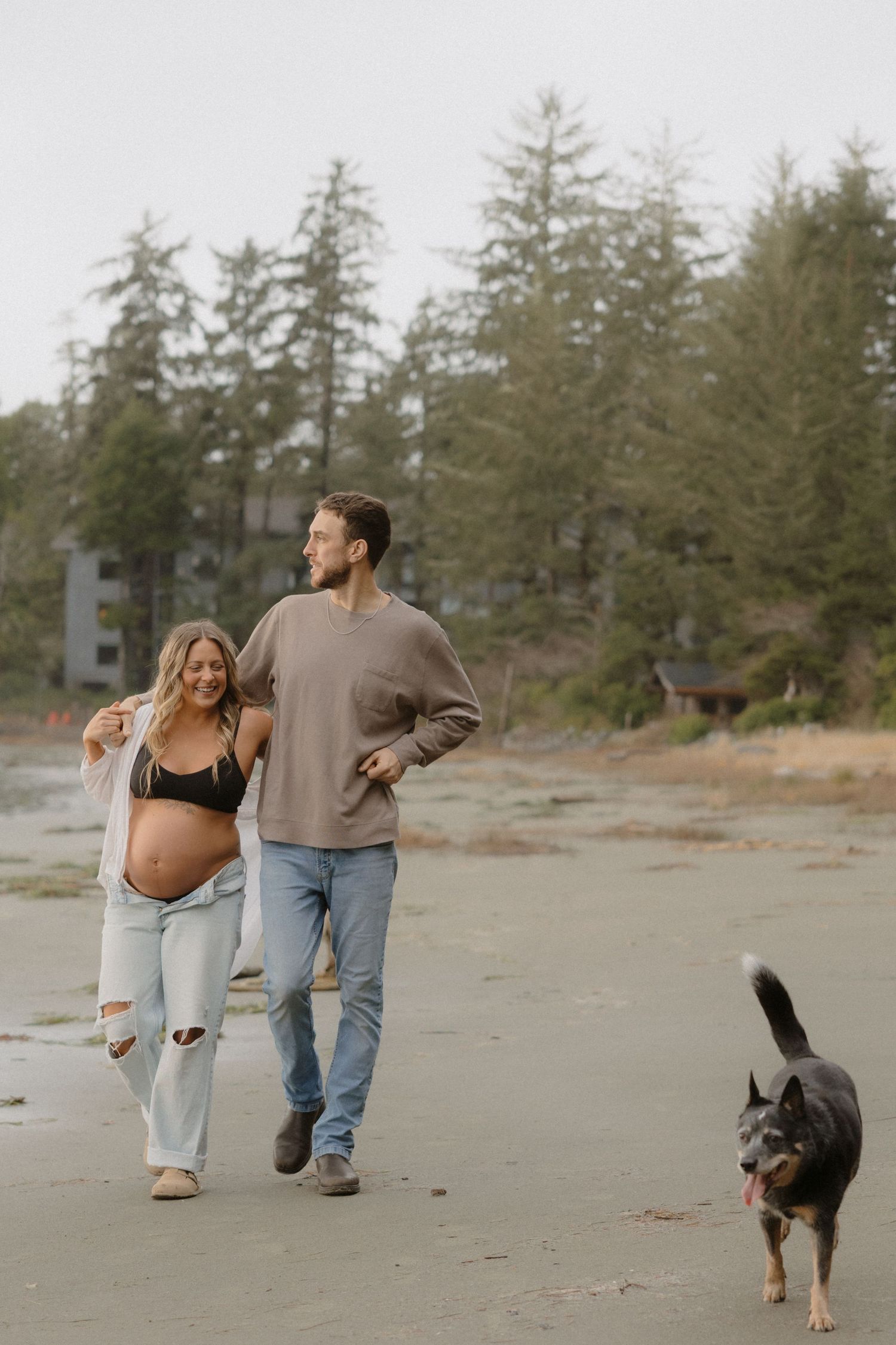 A couple walks their dog along a scenic beach during their maternity photoshoot.