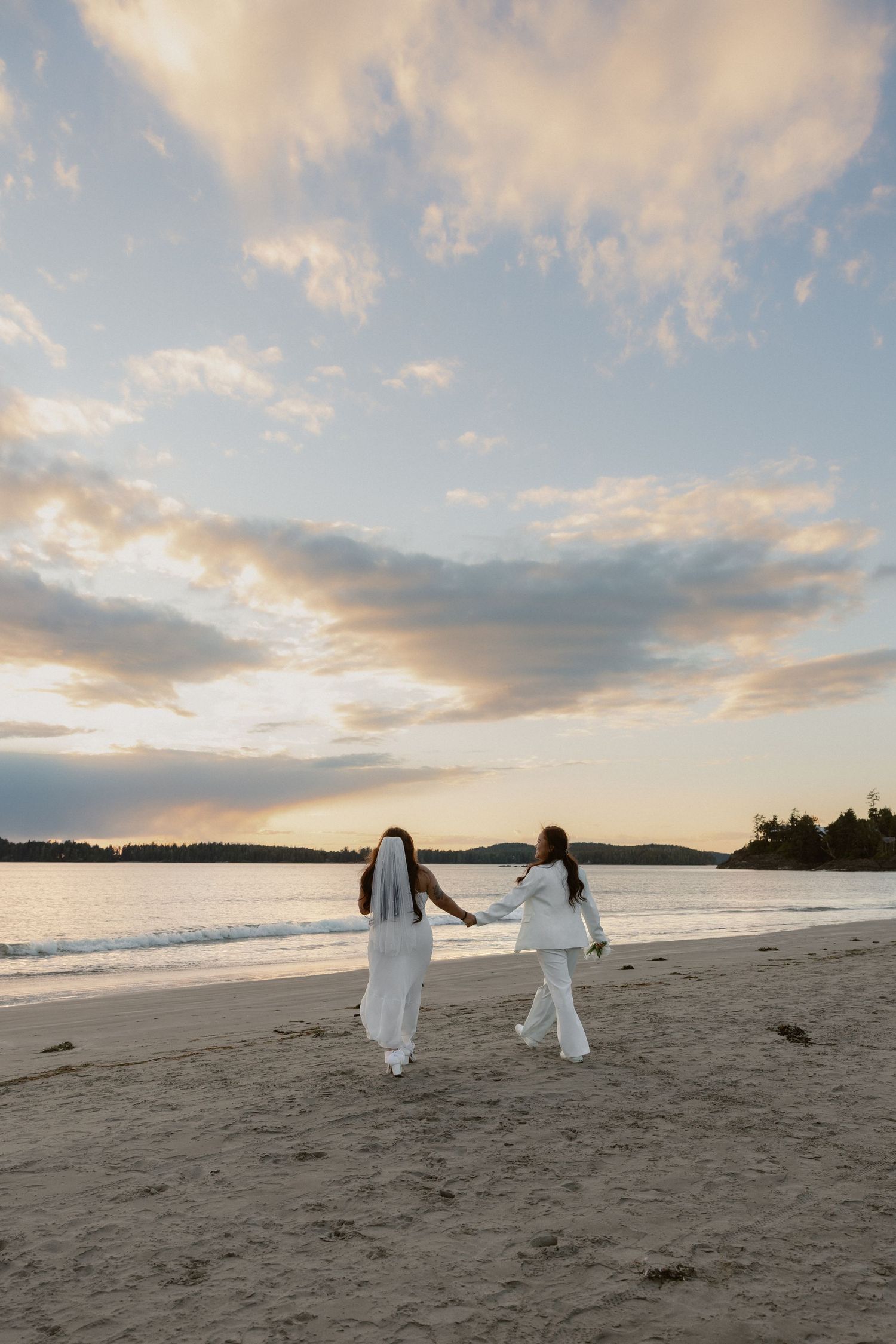 Wide beach landscape at sunset with two figures in white walking in the distance.