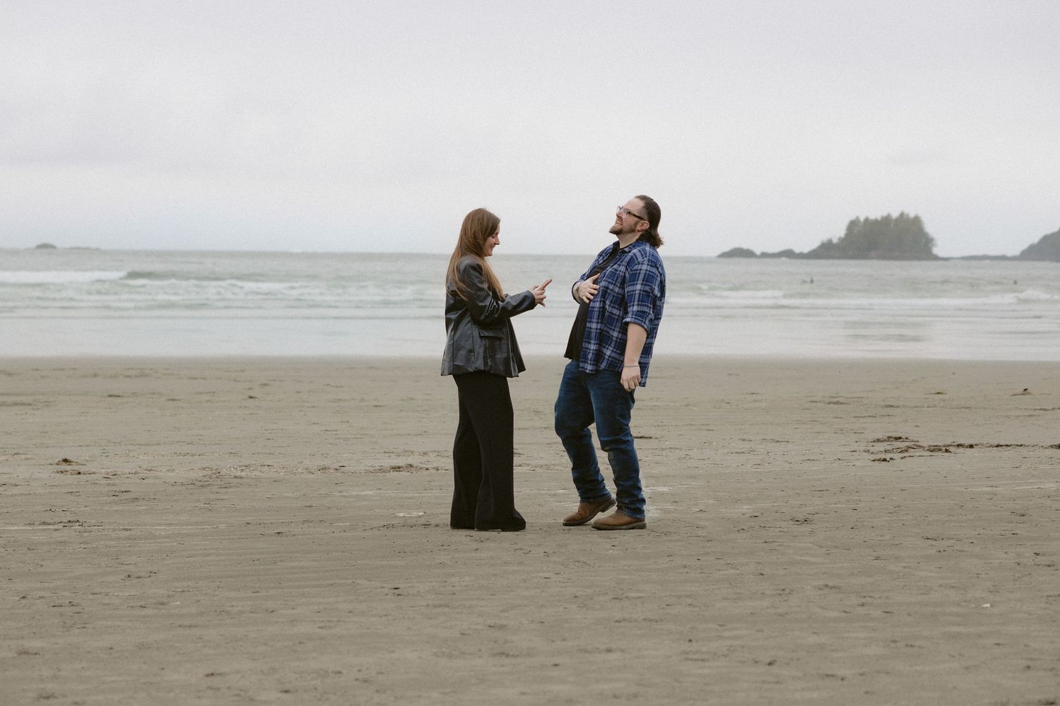 Two people walking together on a wide sandy beach with coastal cliffs in the distance.
