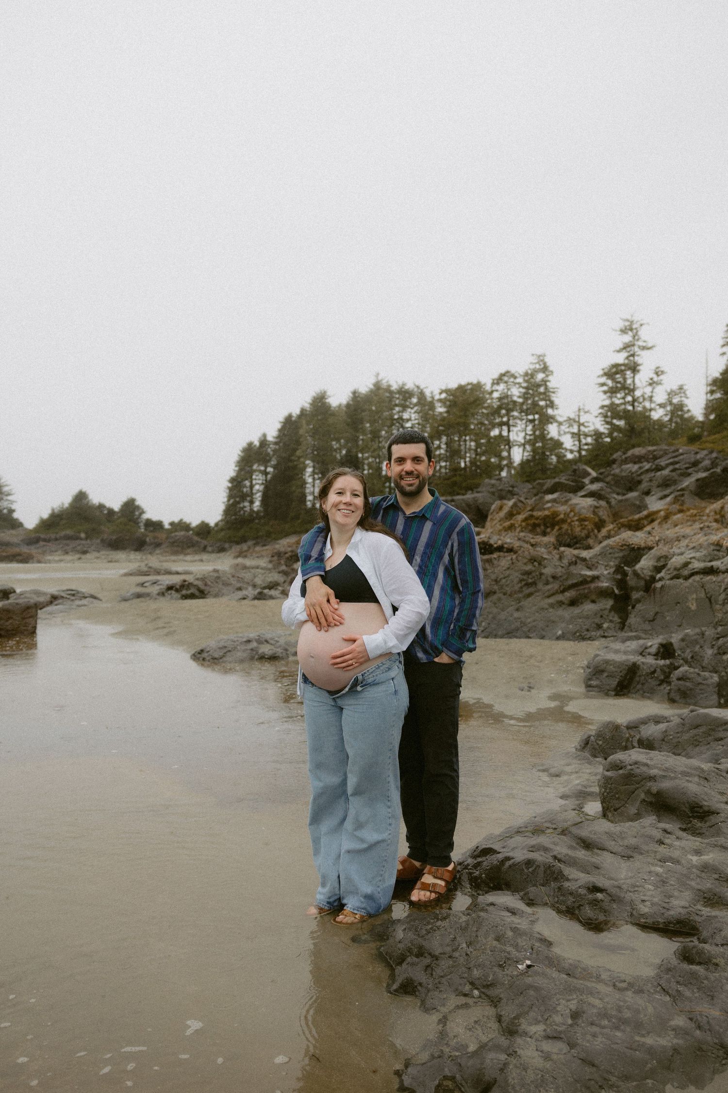 Couple standing together on rocky beach coastline during overcast day.