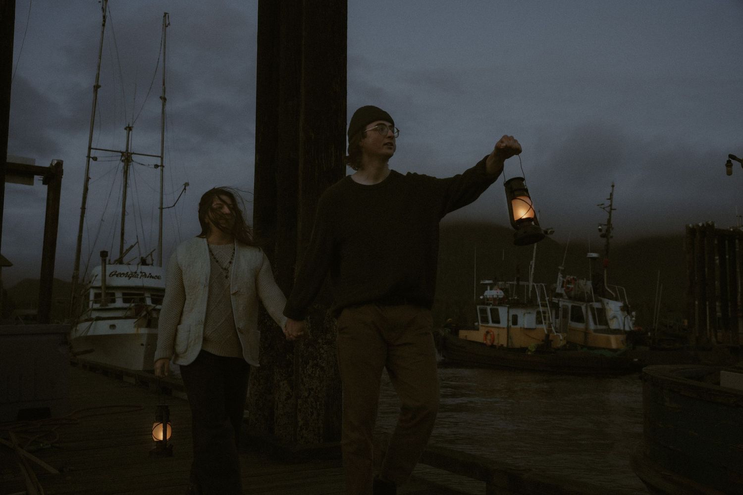 Silhouettes against a dusky sky with boats and dock lights creating a moody atmosphere.