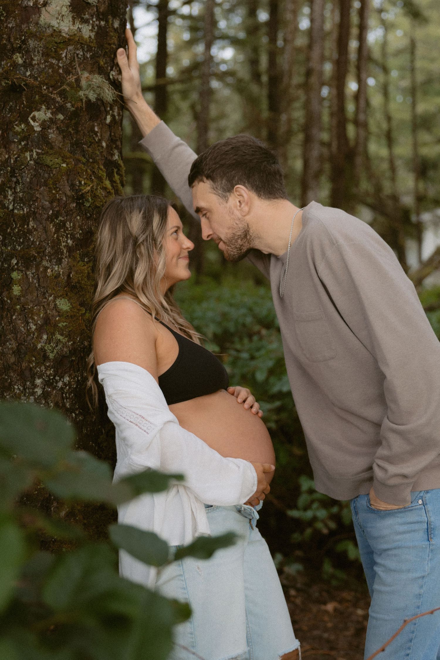 Intimate couple poses among trees in a forest setting.